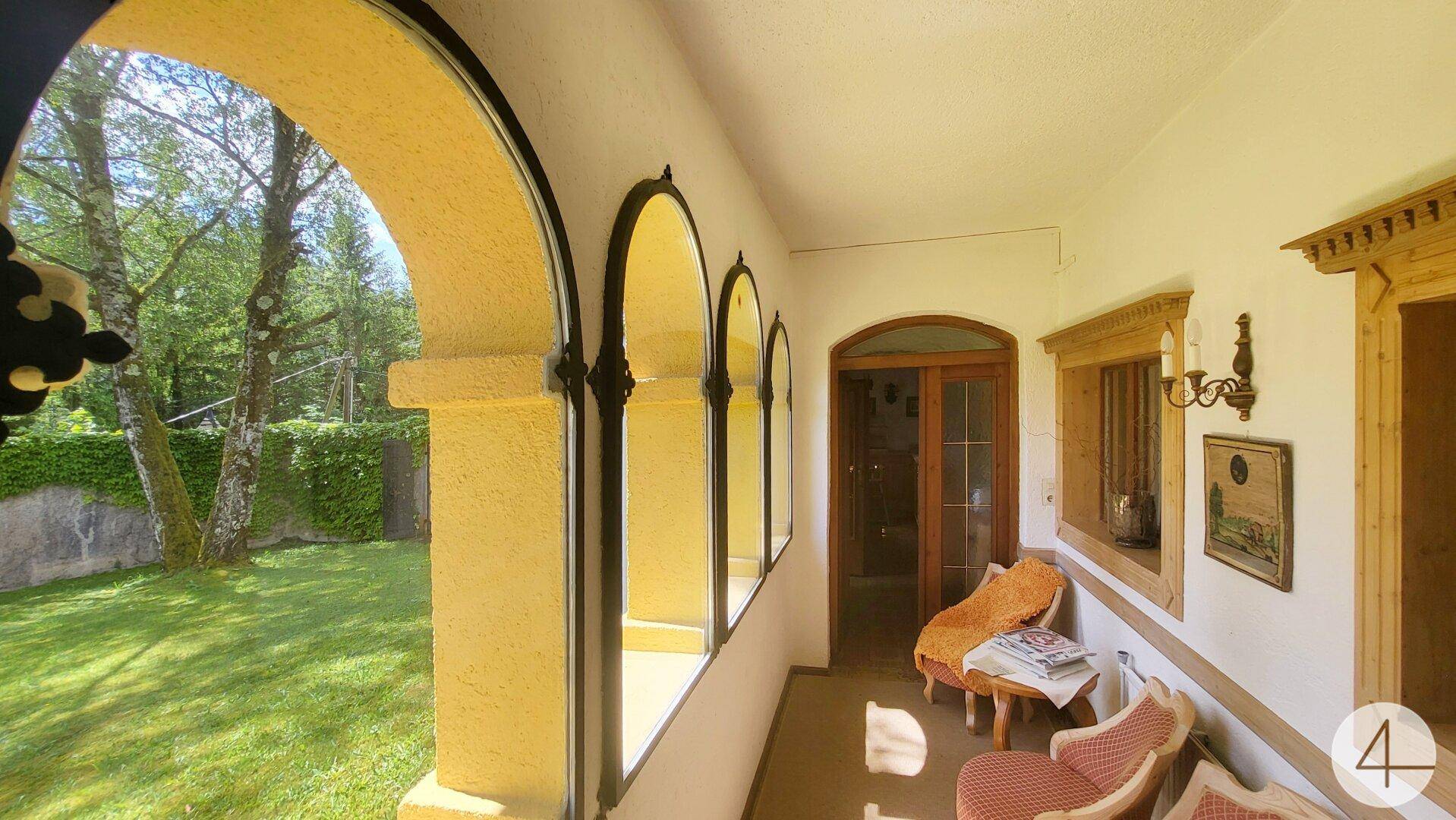 Gemütliche Loggia mit traditionellen Möbeln und Blick auf den grünen Gartenbereich.
