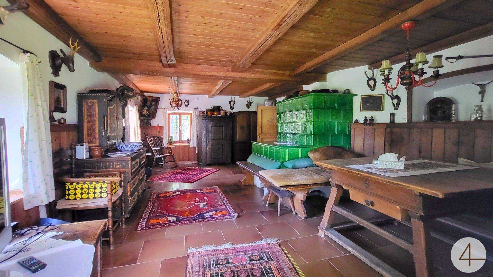 Traditioneller Wohn- und Essbereich mit Holzbalkendecke, Kachelofen und rustikalen Möbeln.