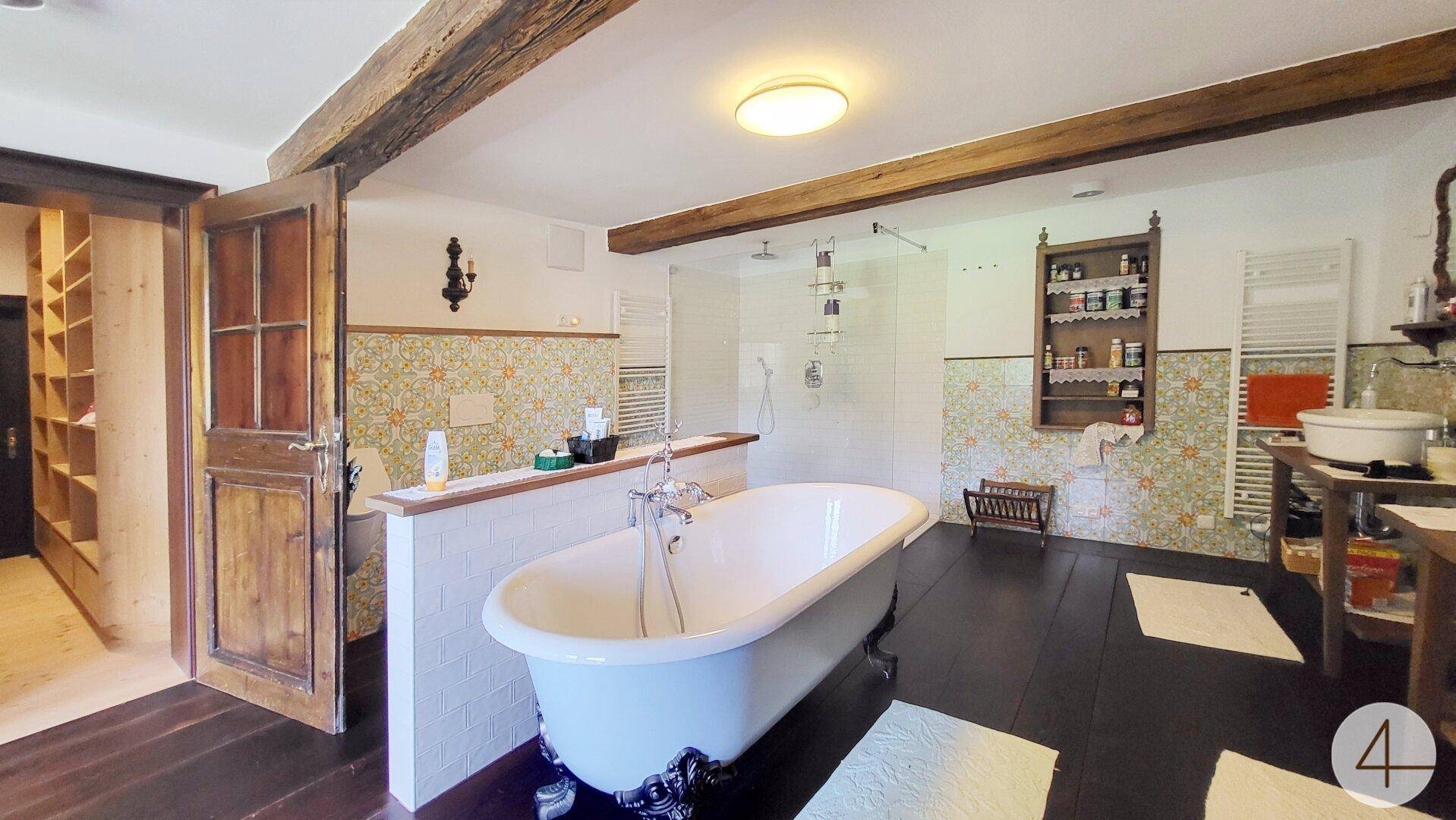 Geräumiges Badezimmer mit freistehender Badewanne, Dusche und Holzbalken, die rustikalen Charme verleihen.