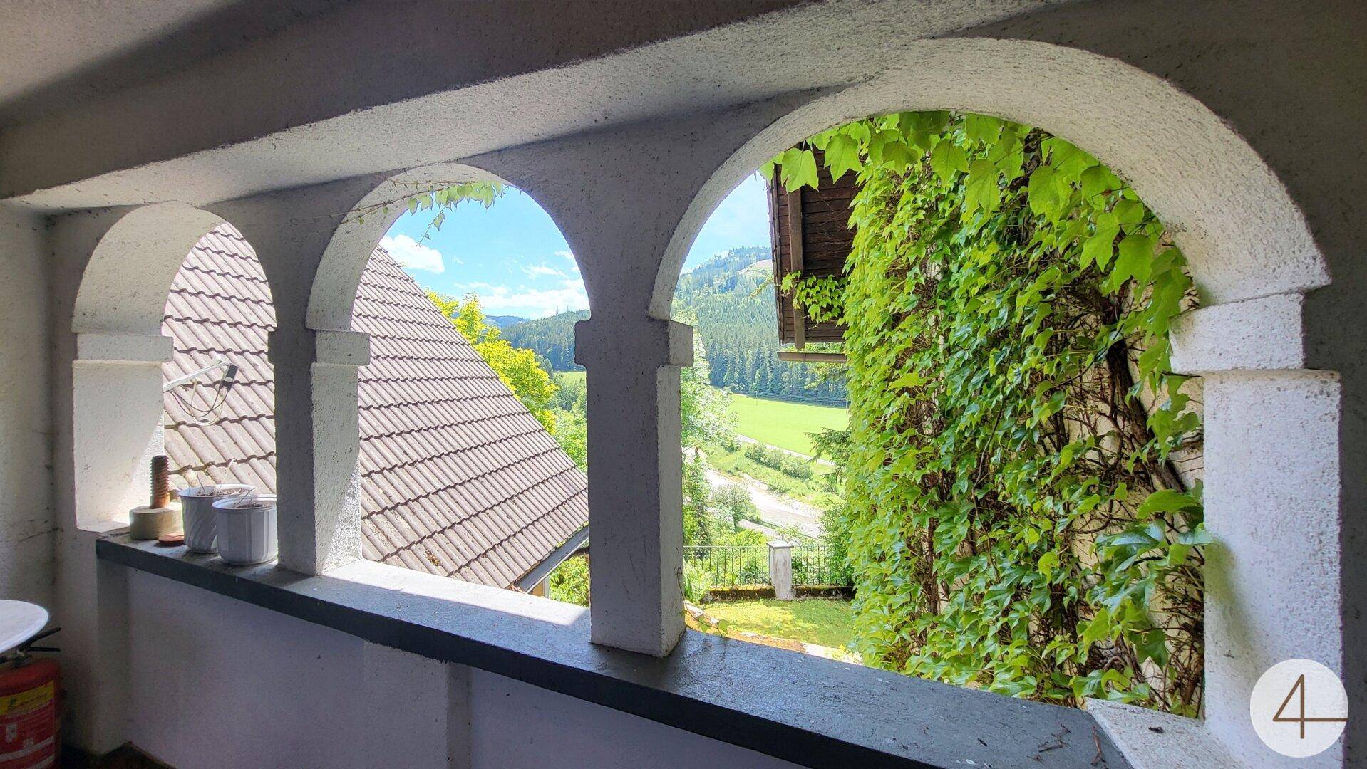 Malerischer Ausblick durch Rundbogenfenster auf die grüne Hügellandschaft und das Tal.