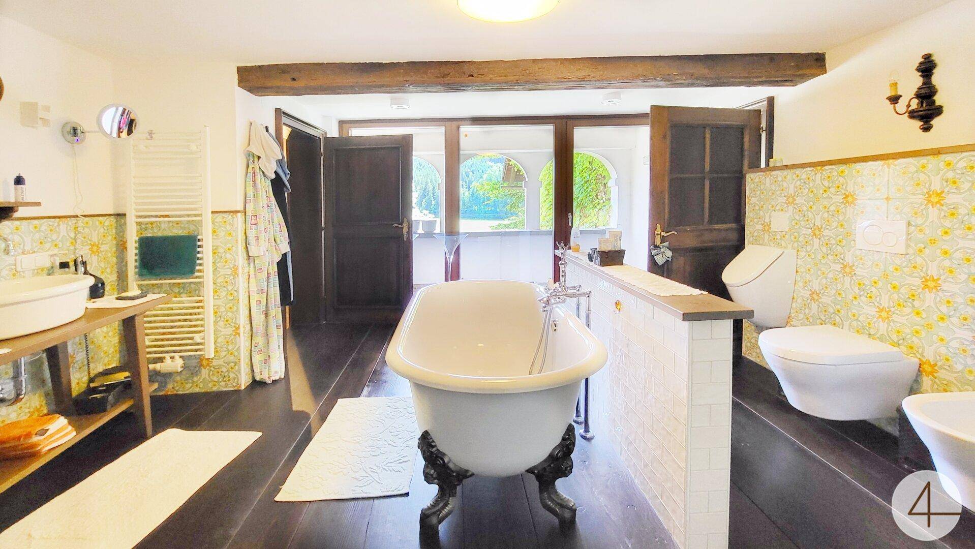 Geräumiges Badezimmer mit freistehender Badewanne, Holzbalken und traditionellen Fliesen.