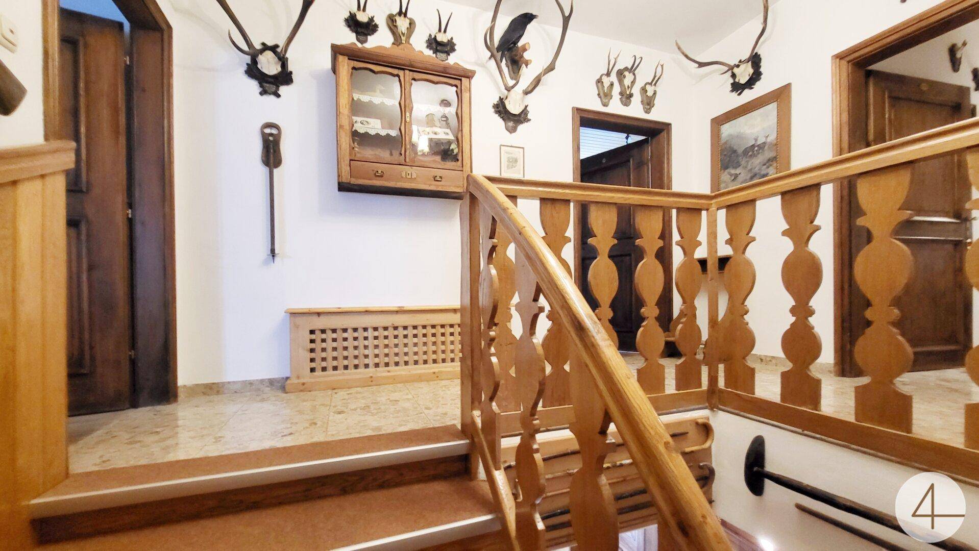 Treppenhaus mit Holzgeländer, Jagdtrophäen und traditionellen Holzelementen.