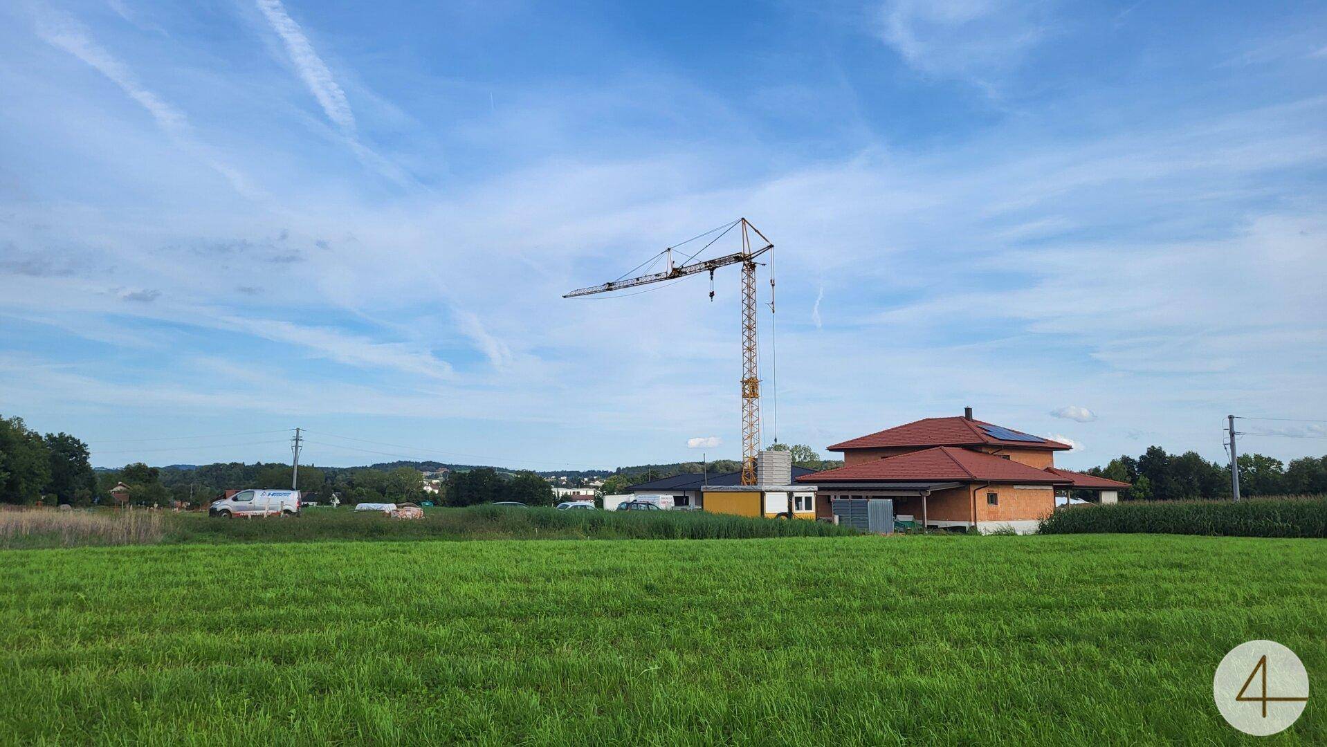 Weitläufiges grünes Feld mit einem Haus mit Solaranlage und einem Baukran am Horizont.