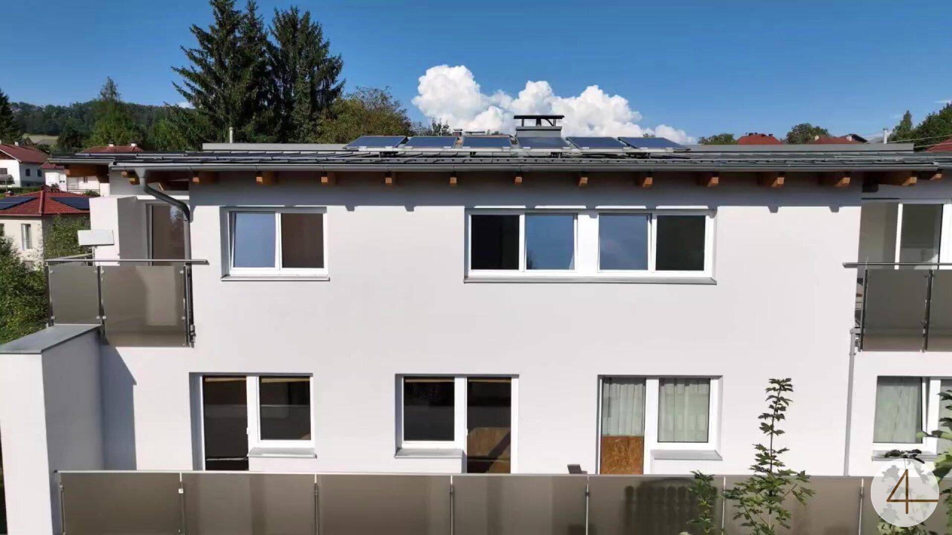 Nahaufnahme der Gebäudefassade mit Balkonen, Fenstern und sichtbaren Solarpaneelen auf dem Dach.