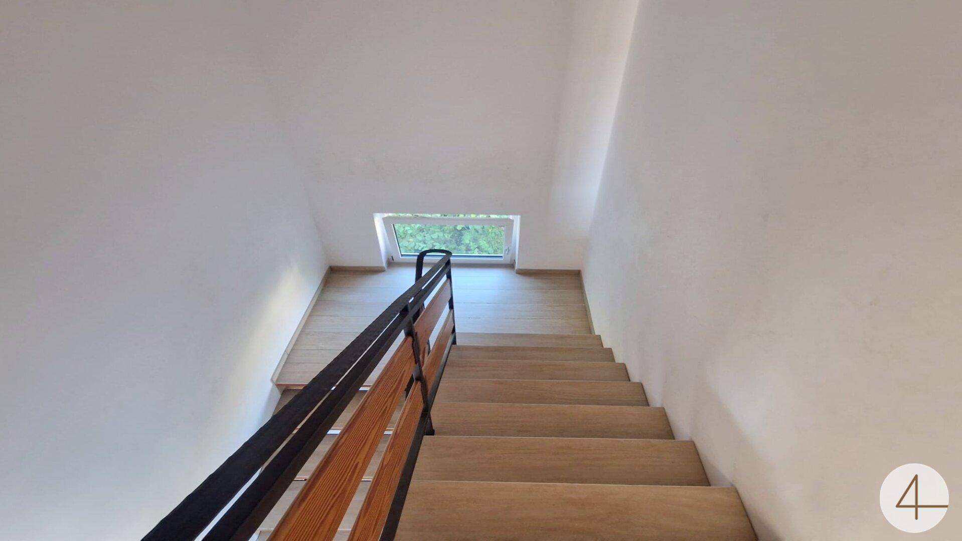 Heller Treppenaufgang mit Holzstufen, modernem Geländer und Oberlicht für natürliches Licht.