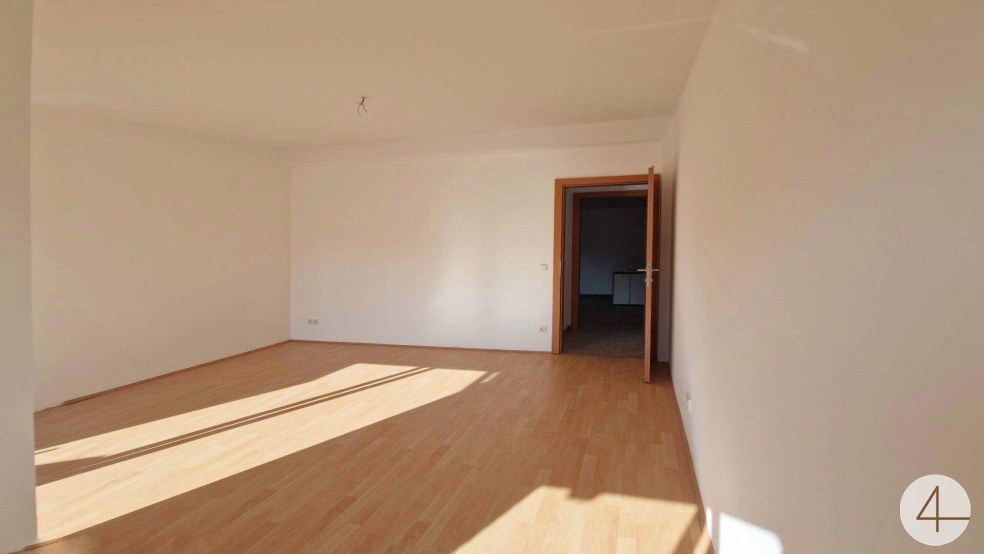 Geräumiges, helles Zimmer mit Holzboden und Türzugang, ideal für Wohn- oder Schlafbereich.