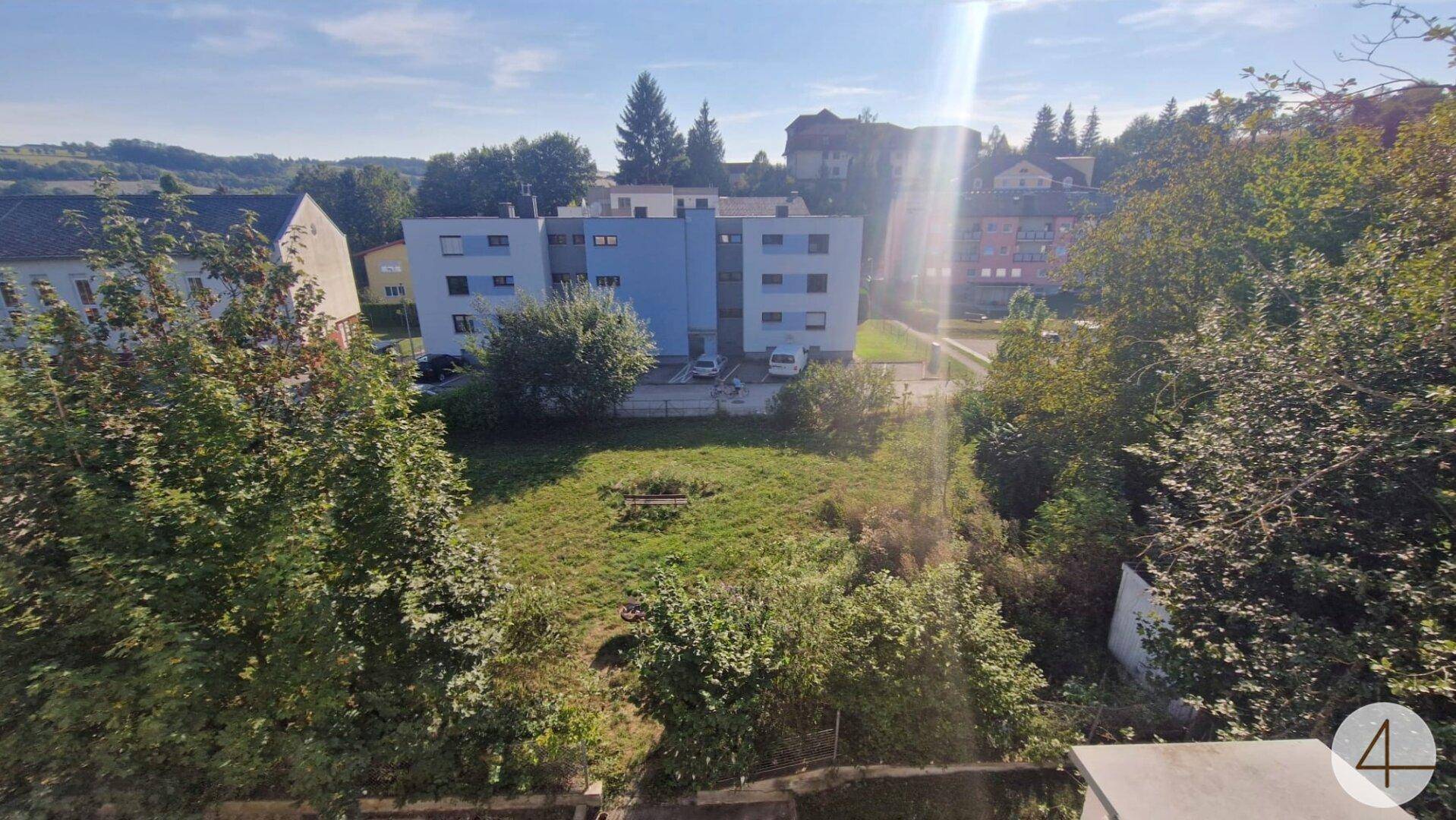 Weitläufiger Blick ins Grüne mit umliegenden Gebäuden unter strahlend blauem Himmel.