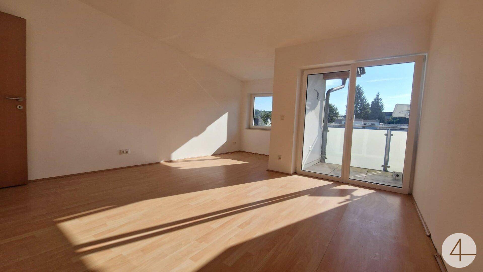 Helles Zimmer mit Holzboden, Dachschräge und Balkonzugang, sonnendurchflutet.