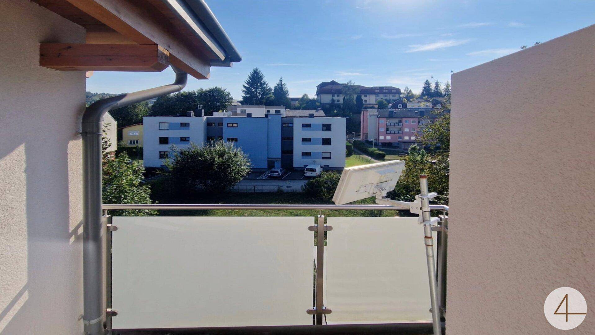 Balkon mit Glasgeländer und Blick auf die umliegende Wohngegend und viel Grün.