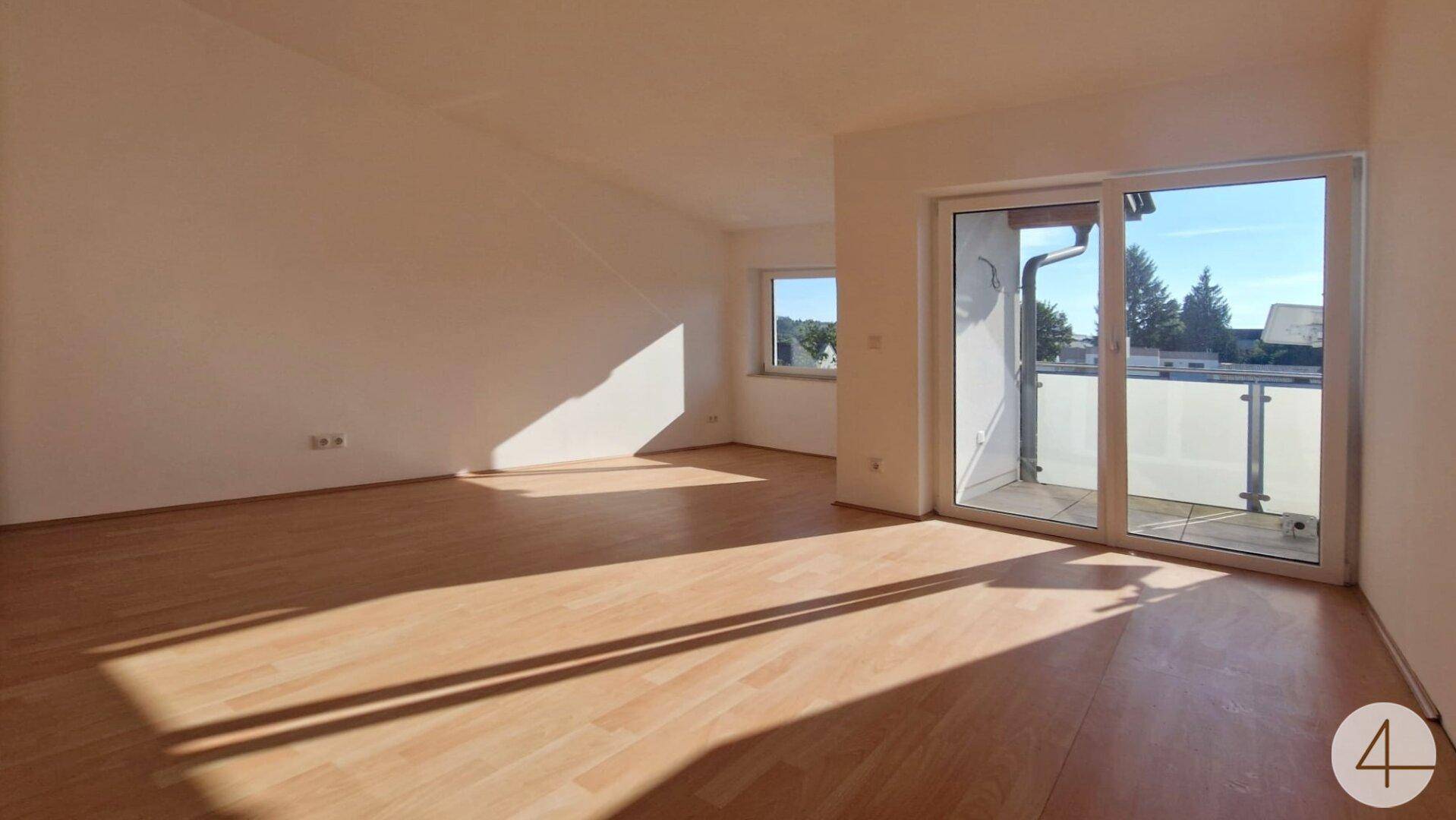 Helles Zimmer mit Holzboden, Dachschräge und Balkonzugang, sonnendurchflutet.