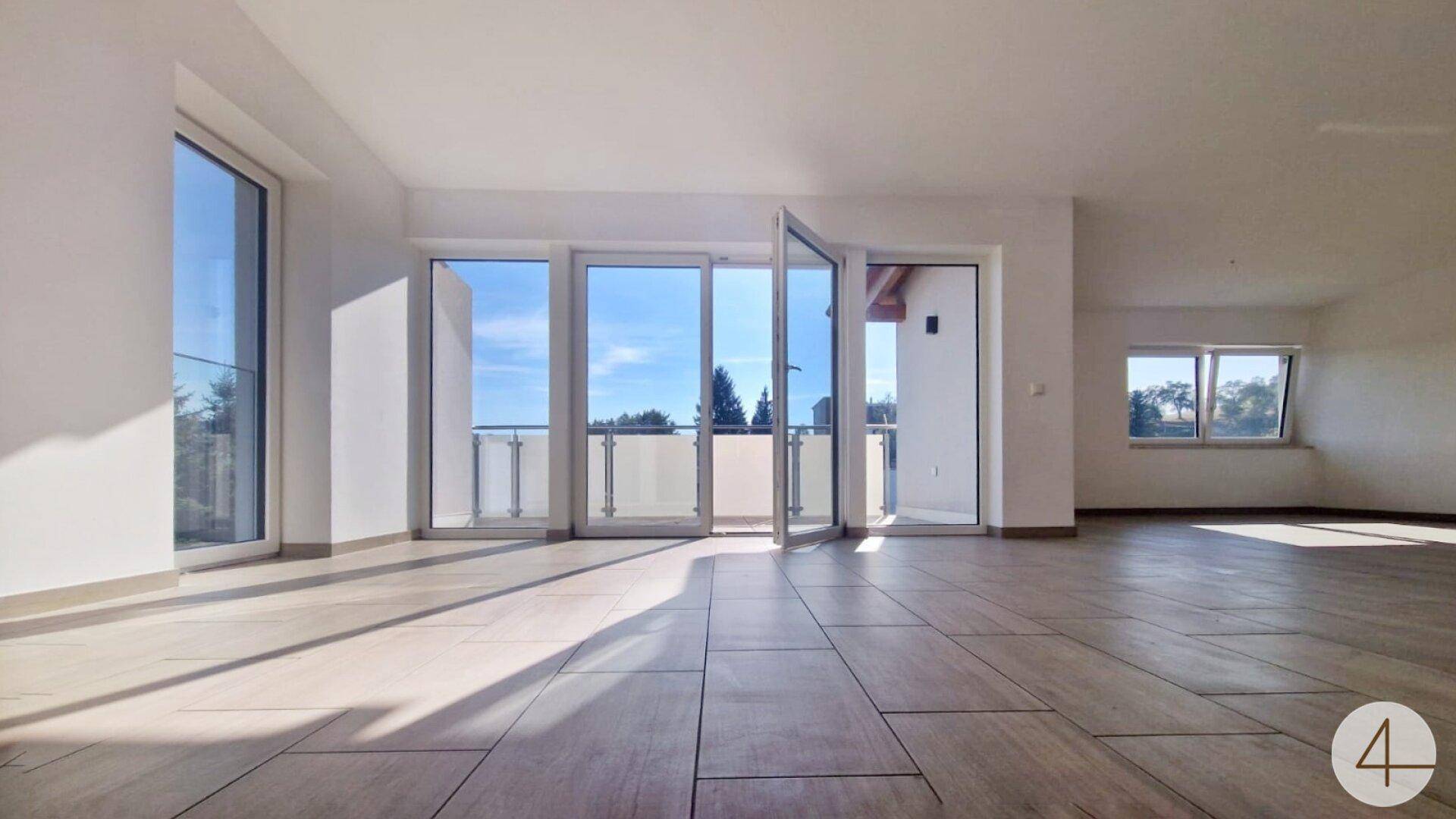 Großer, heller Raum mit Fliesenboden und mehreren Balkonzugängen, lichtdurchflutet.