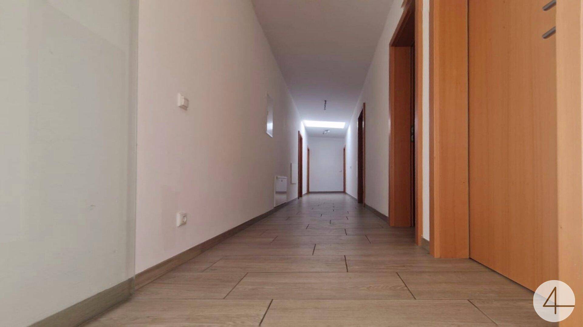 Langer, heller Flur mit Fliesenboden und Holztüren, der zu verschiedenen Räumen führt.