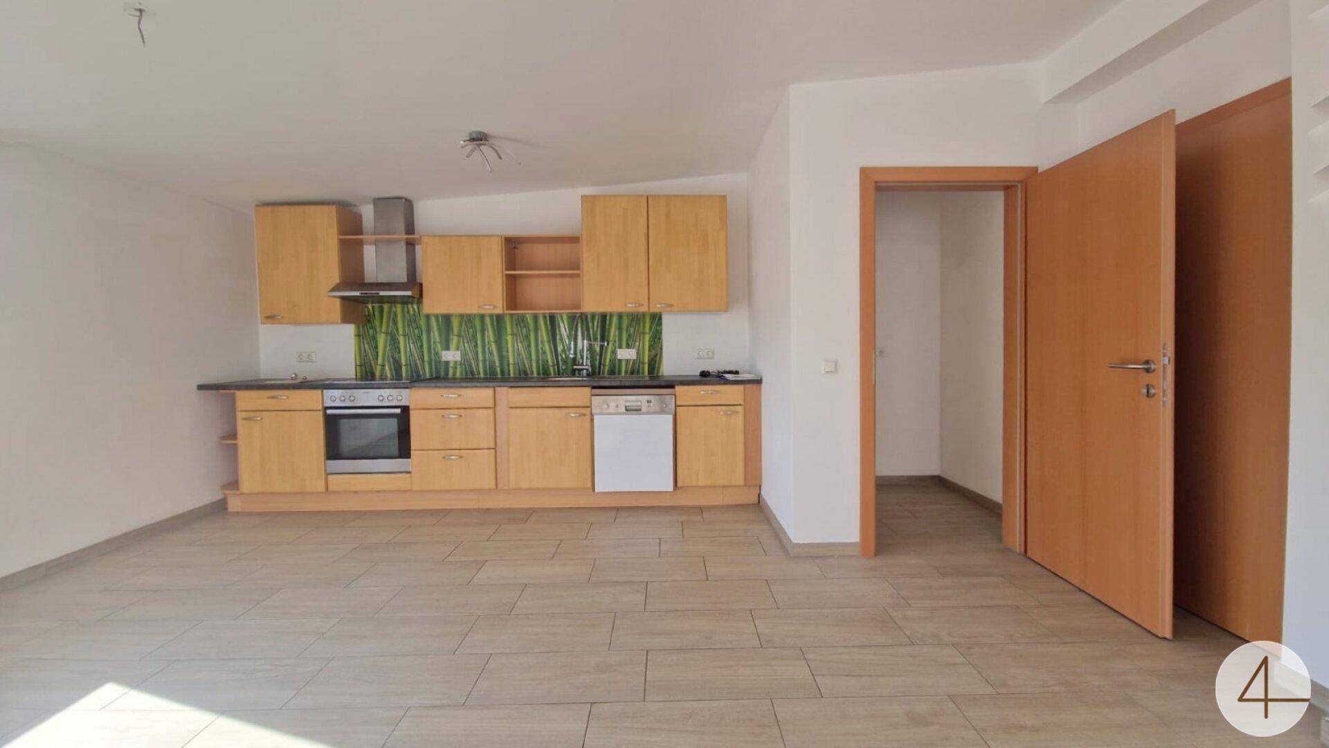 Funktionale Einbauküche mit Holzfronten, Geräten und grünem Fliesenspiegel in hellem Raum.