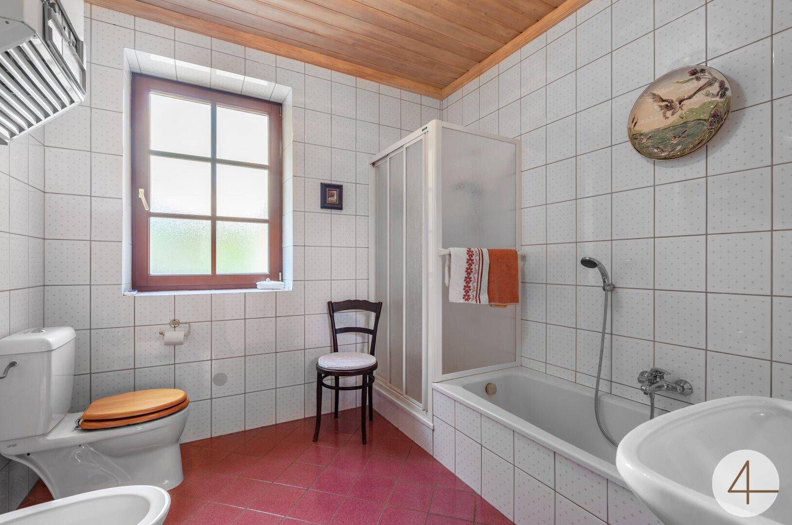 Helles Badezimmer mit weißen Fliesen, Badewanne, Dusche und Fenster.
