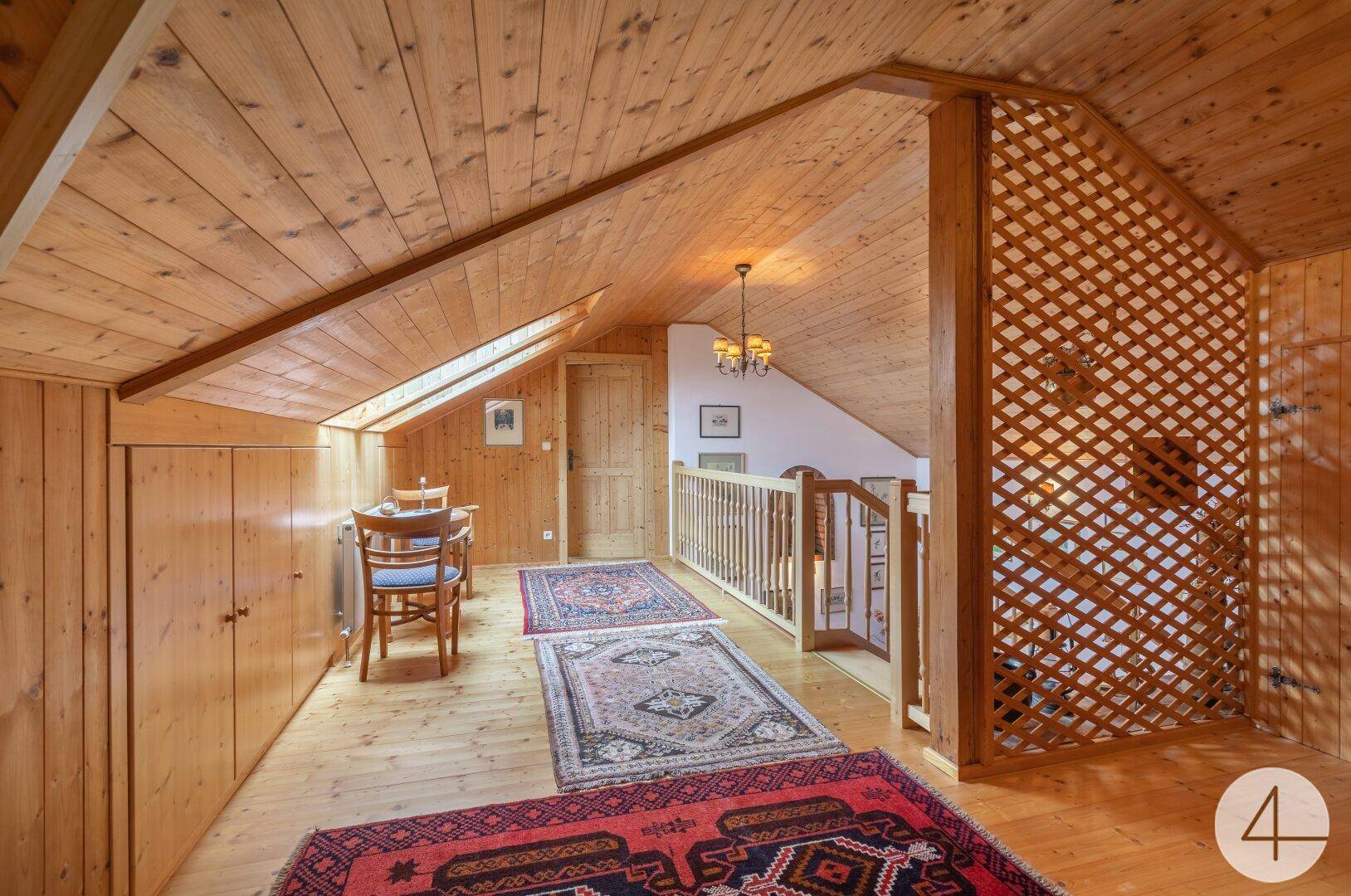Gemütlicher Flurbereich im Dachgeschoss mit Holzverkleidung, Teppichen und kleiner Sitzecke.