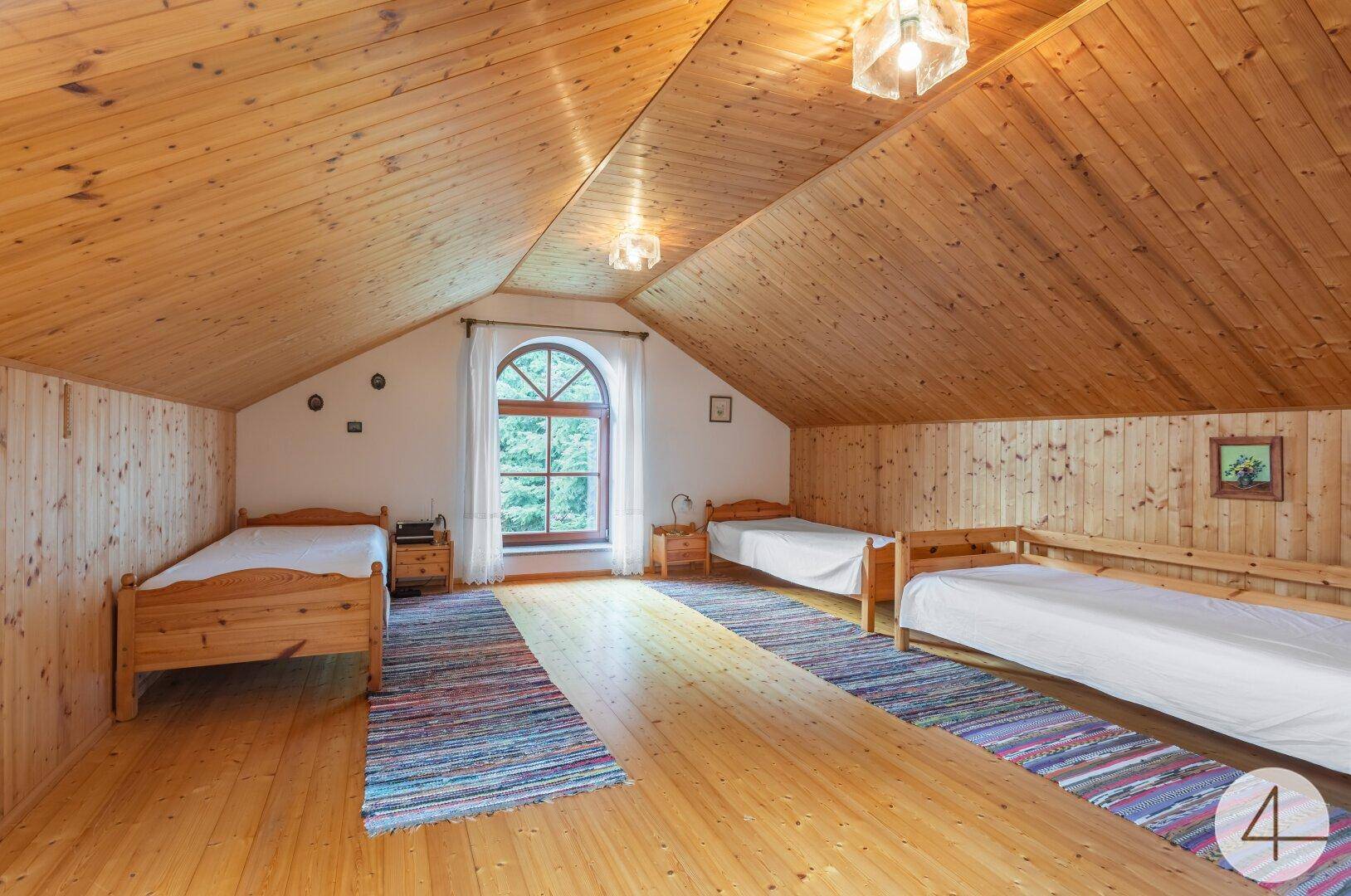 Geräumiges Schlafzimmer im Dachgeschoss mit Holzverkleidung, mehreren Betten und Rundbogenfenster.