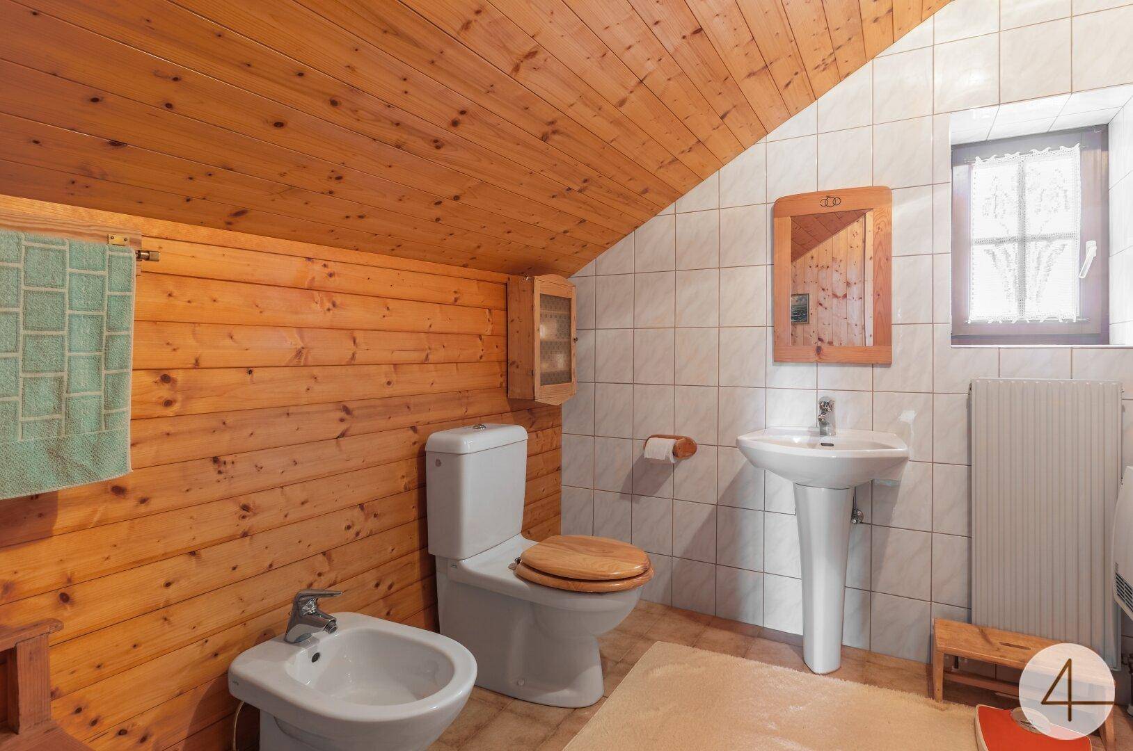Badezimmer im Dachgeschoss mit Holzverkleidung, weißen Fliesen, Bidet und Fenster.