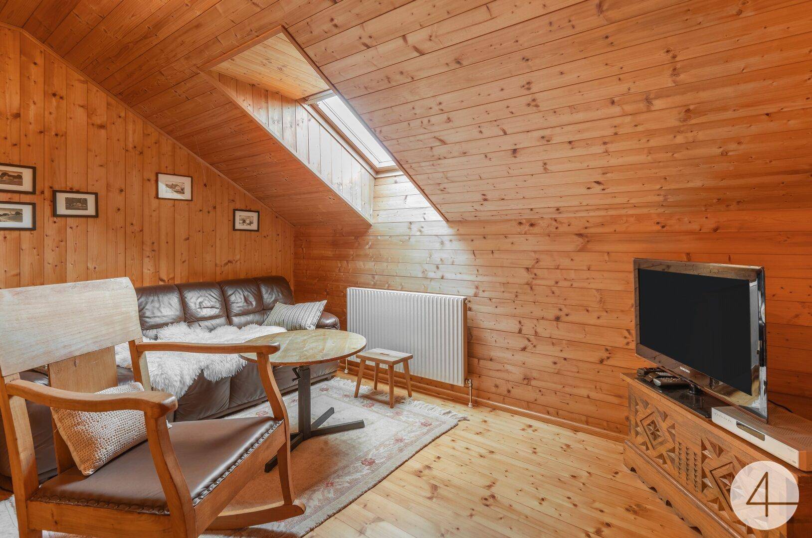 Gemütlicher Wohnbereich im Dachgeschoss mit Holzverkleidung, Sofa und Fernseher.