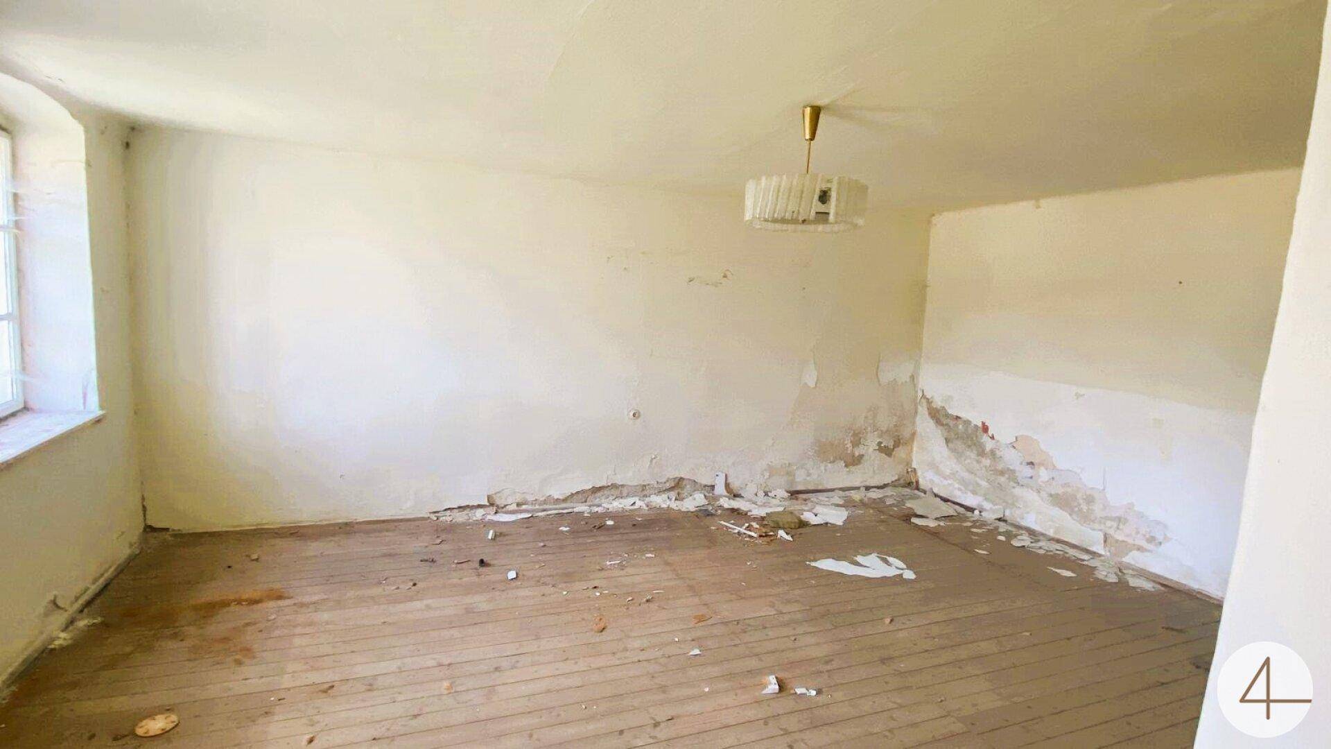 Leerer Raum mit abgenutztem Holzboden, abblätternder Farbe an den Wänden und einem Fenster für natürliches Licht.