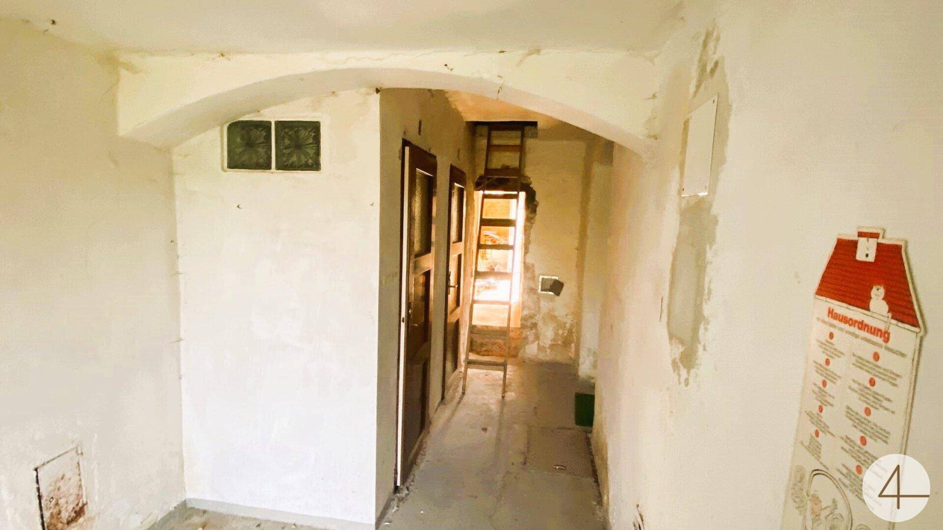 Langer Flur mit gewölbter Decke, mehreren Türen und einem Schild an der Wand, der Renovierung benötigt.