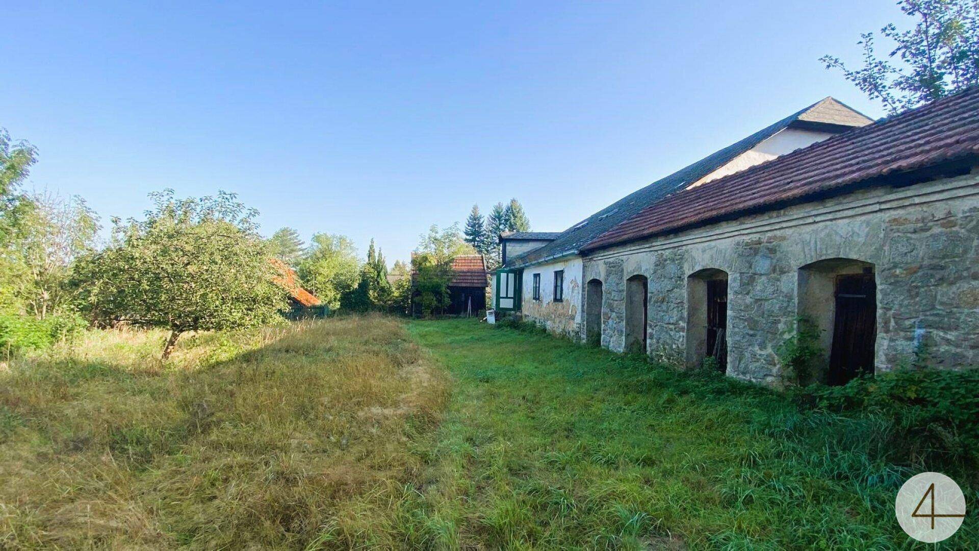 Historisches Gebäude mit markanten Steinbögen und einer langen, grasbewachsenen Fläche davor unter blauem Himmel.