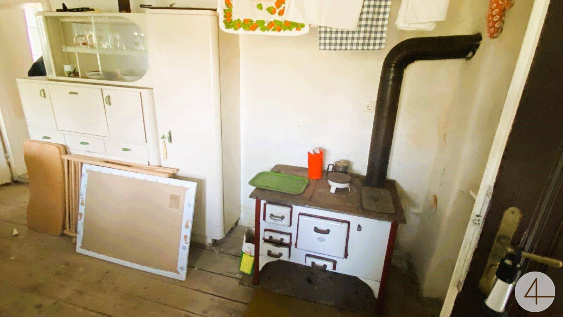 Einfacher Hauswirtschaftsraum mit altem Holzofen, Schränken und Wäscheleinen, der eine Modernisierung benötigt.