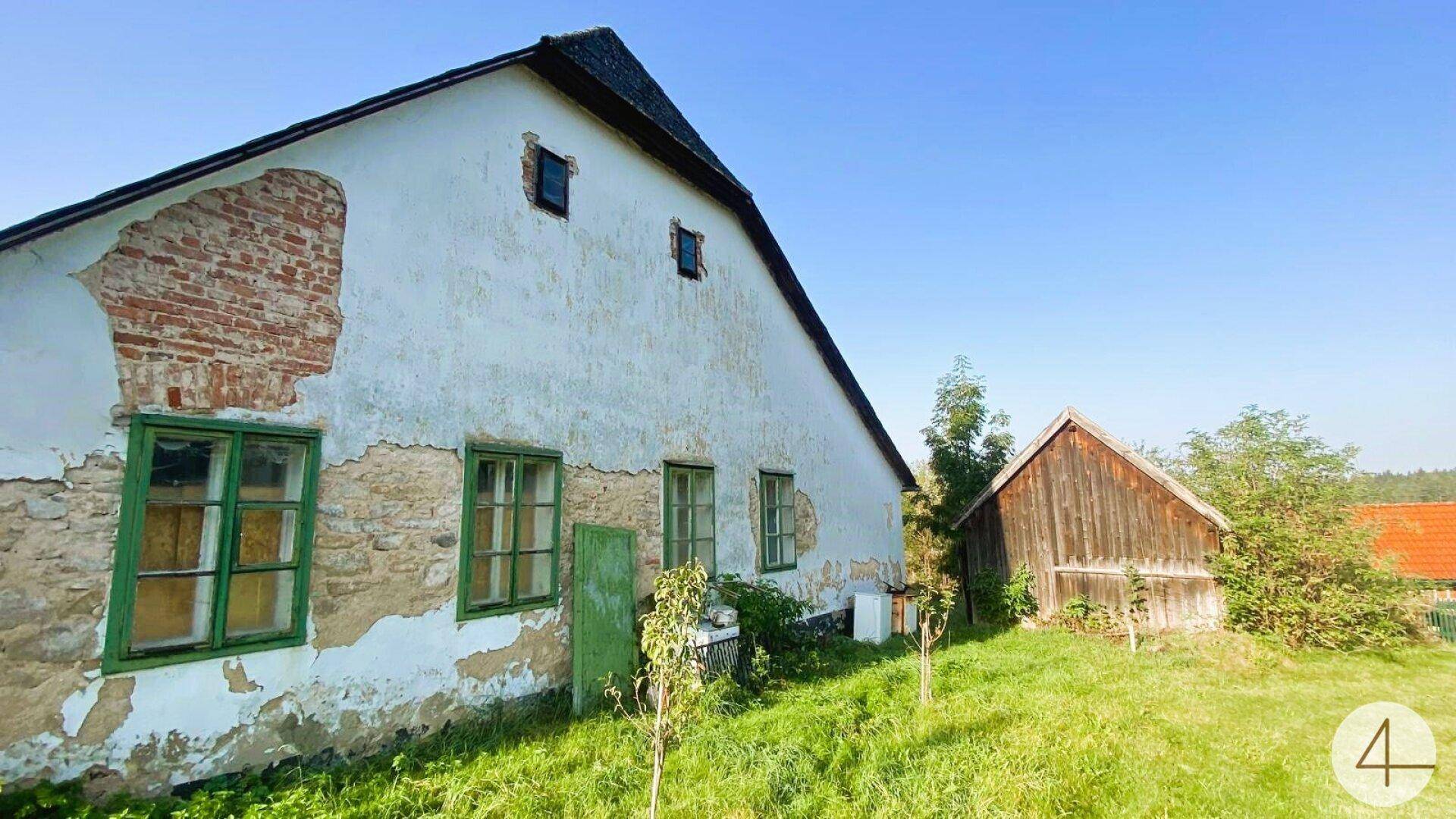 Detailansicht eines alten Bauernhauses mit sichtbaren Ziegeln und grünen Fensterrahmen unter blauem Himmel.