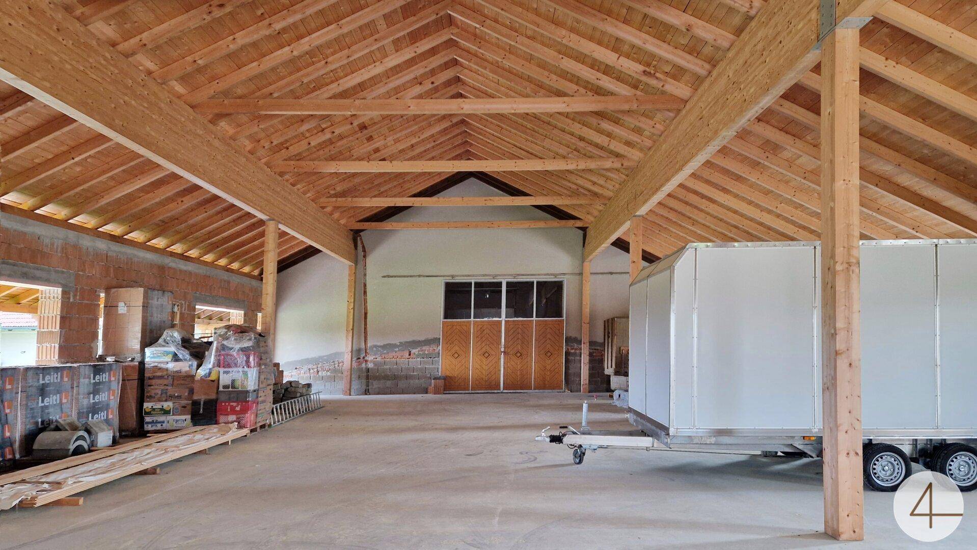 Großer, offener Raum im Rohbau mit sichtbaren Holzbalken und Dachkonstruktion, bereit für den Ausbau.