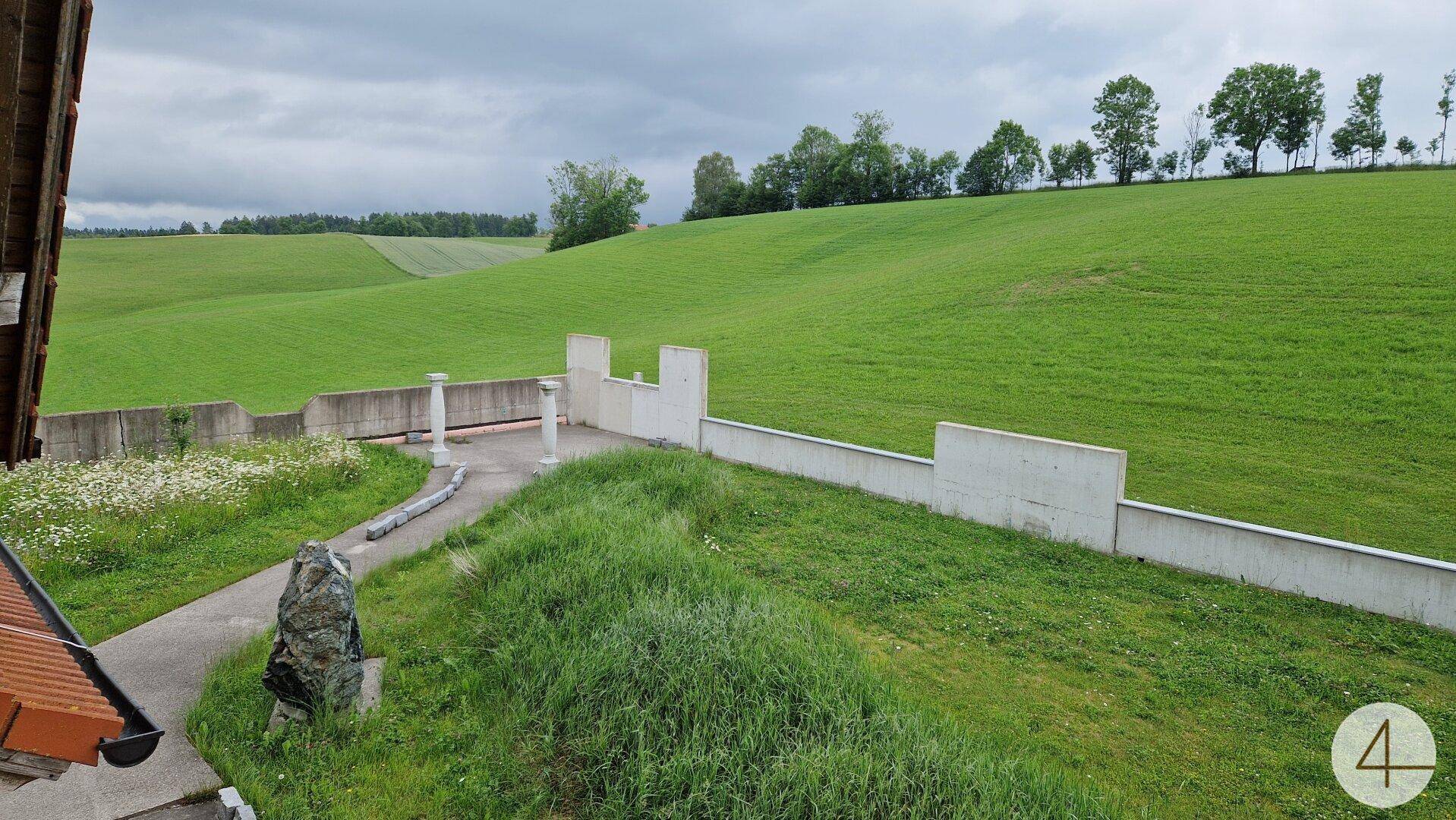 Weitläufiger Blick auf grüne Wiesen und sanfte Hügel unter einem bewölkten Himmel.
