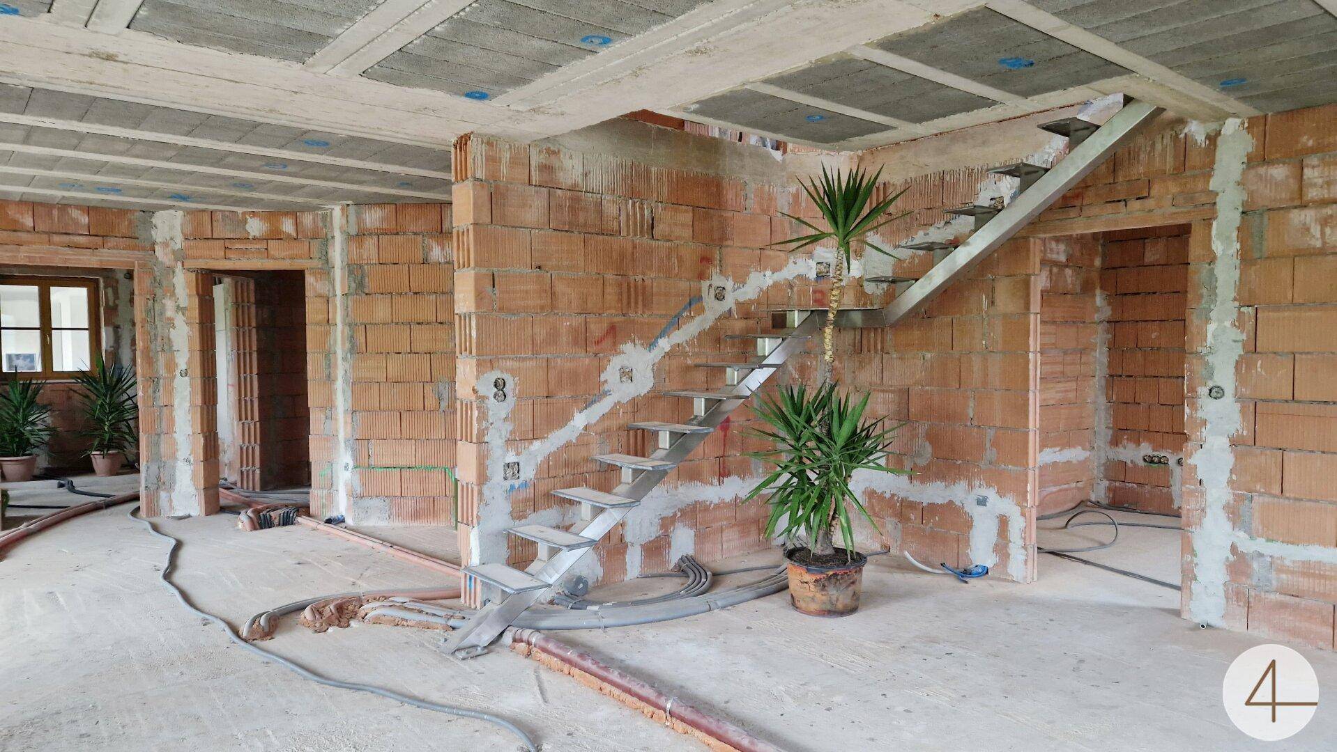 Innenraum im Rohbau mit unverputzten Ziegelwänden, einer modernen Treppe und Betonböden.