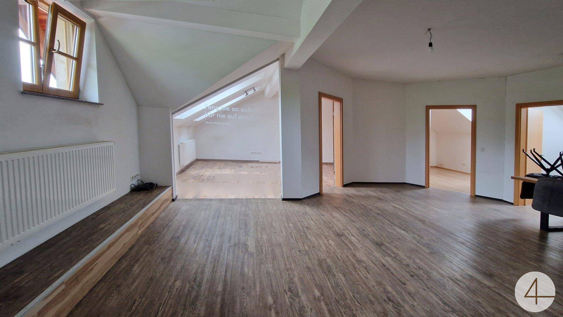 Geräumiger Wohnbereich mit Dachschräge, Laminatboden und mehreren Türen zu angrenzenden Räumen.