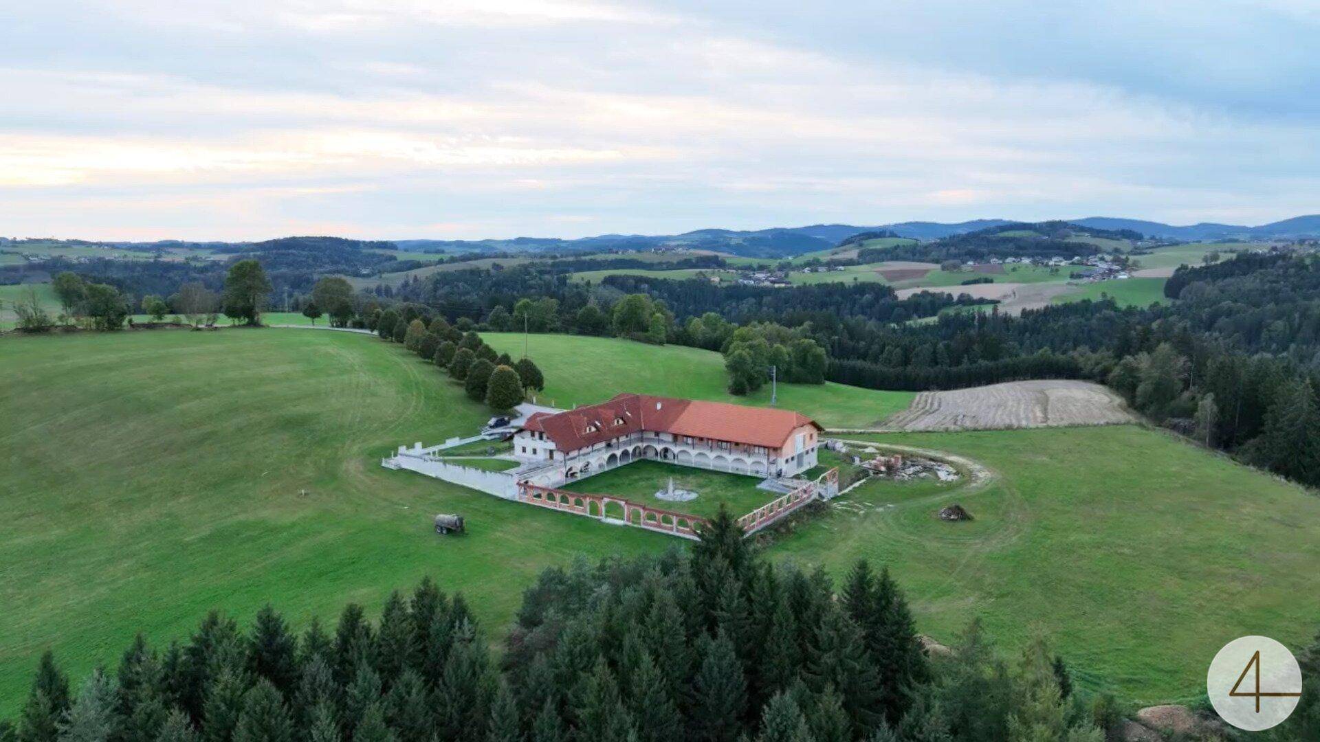 Weitläufige Luftaufnahme des Anwesens mit gepflegtem Innenhof, umgeben von sanften Hügeln und Wäldern.
