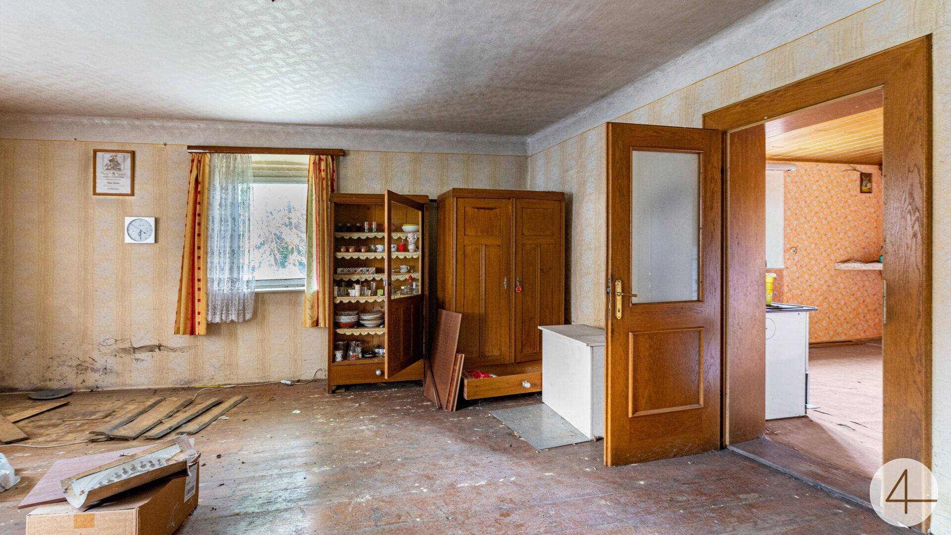 Verwohnter Raum mit alten Holzmöbeln und Blick in einen weiteren Bereich.