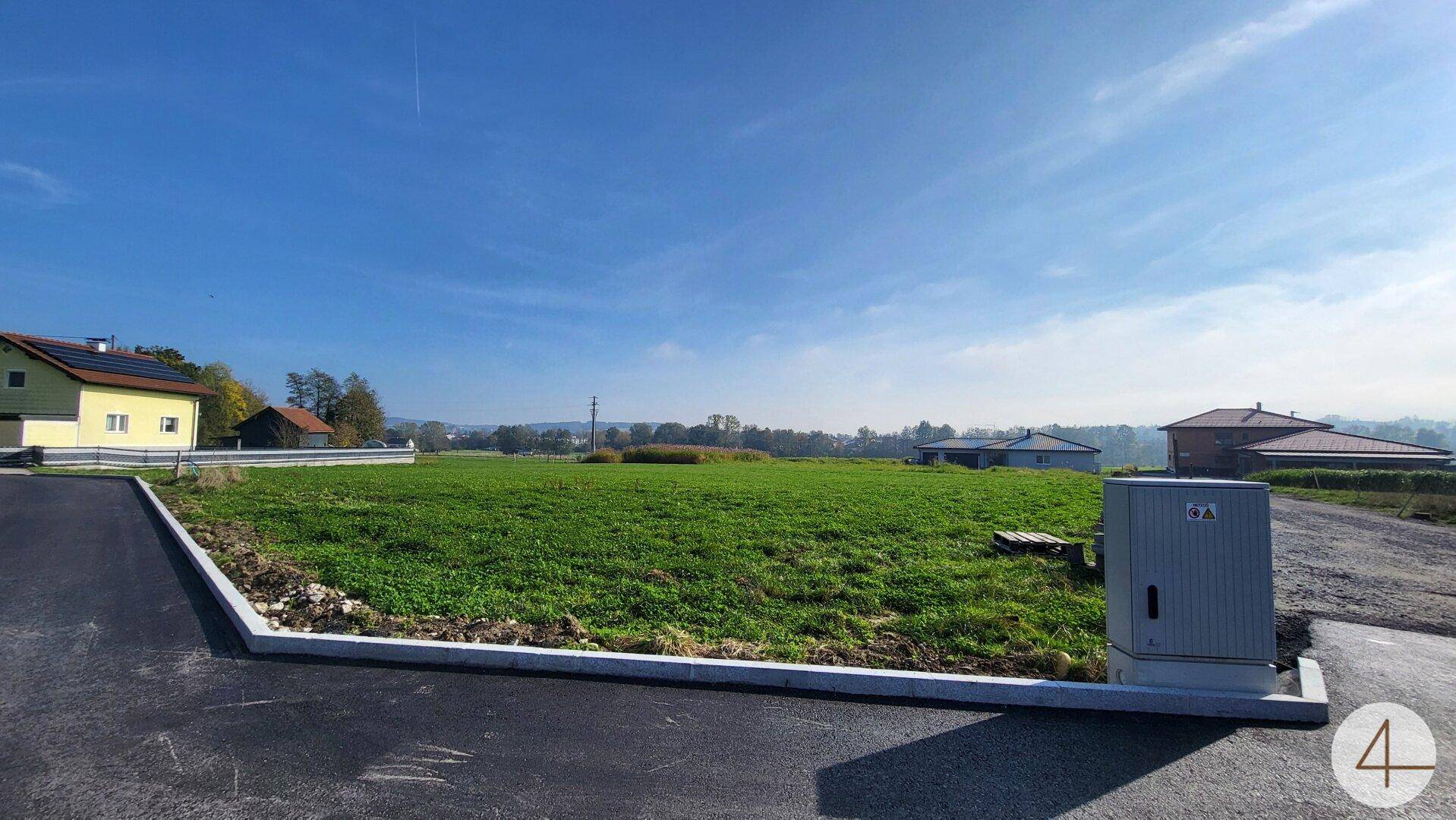 Weitläufiges Grundstück mit grüner Wiese und sonnigem Himmel, umgeben von ländlicher Bebauung.