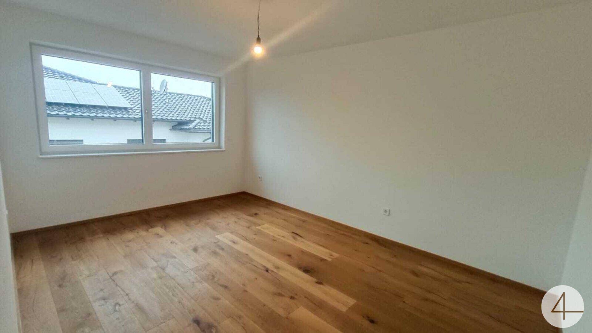 Helles Schlafzimmer mit attraktivem Holzdielenboden und Blick auf die Dächer der Nachbarschaft.