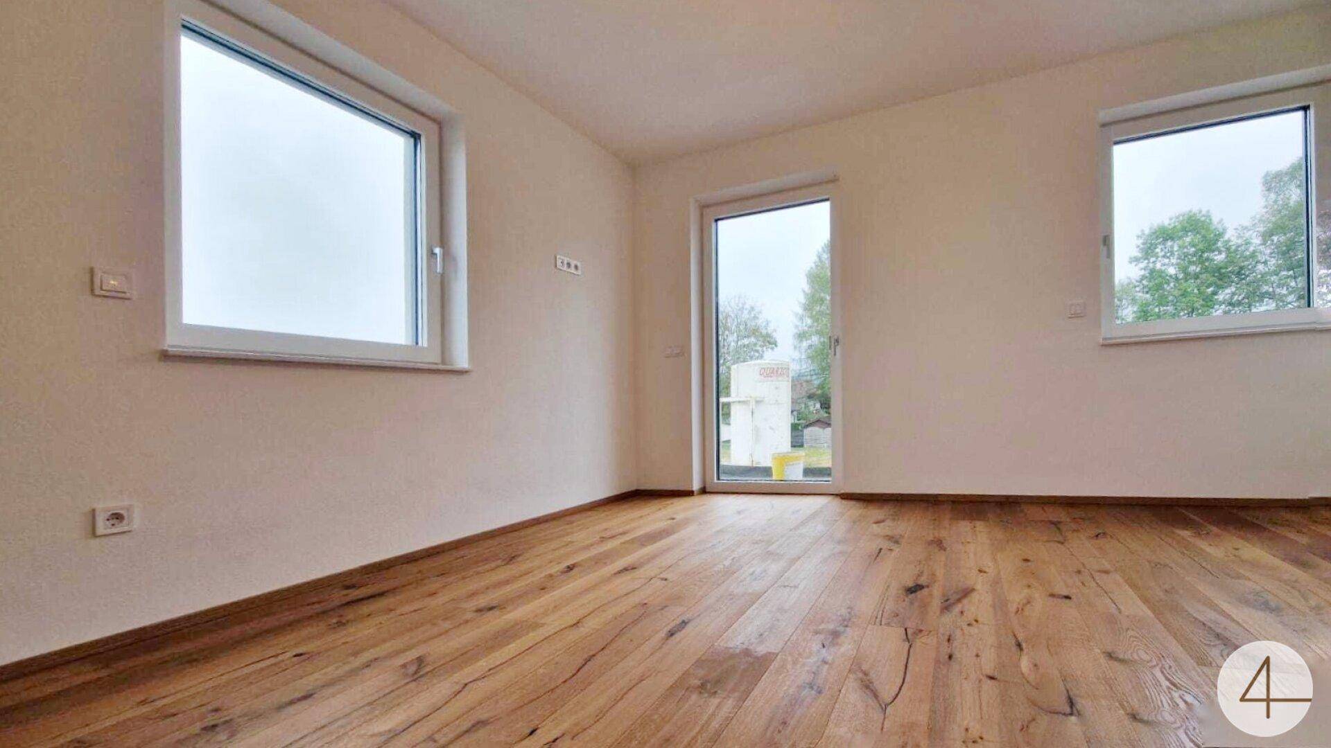 Lichtdurchflutetes Schlafzimmer mit Holzdielenboden, großen Fenstern und Zugang nach draußen.