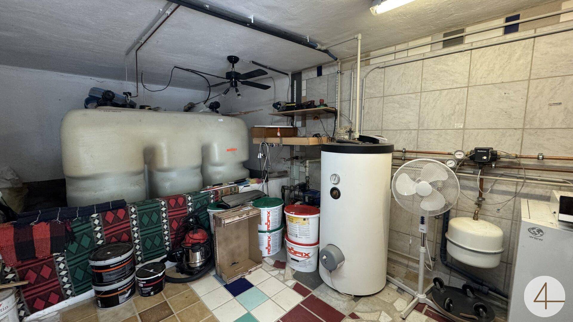 Technikraum im Keller mit Warmwasserspeicher, Wassertanks und Lüfter, funktional eingerichtet.