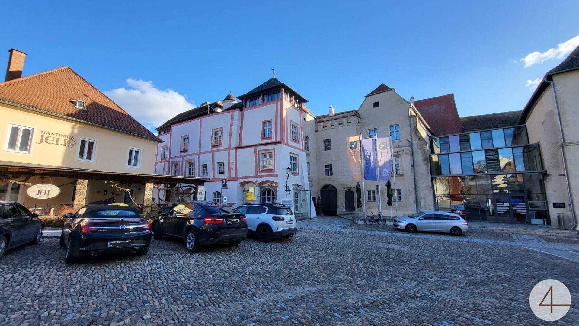 Historisches Gebäude mit markanter Fassade und gepflastertem Vorplatz unter blauem Himmel.