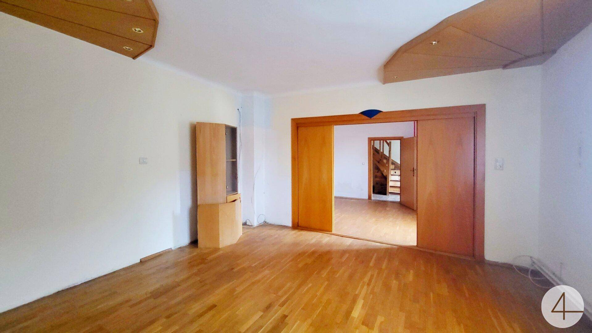 Helles Wohnzimmer mit Parkettboden und Durchgang zu einem weiteren Raum mit Treppe.