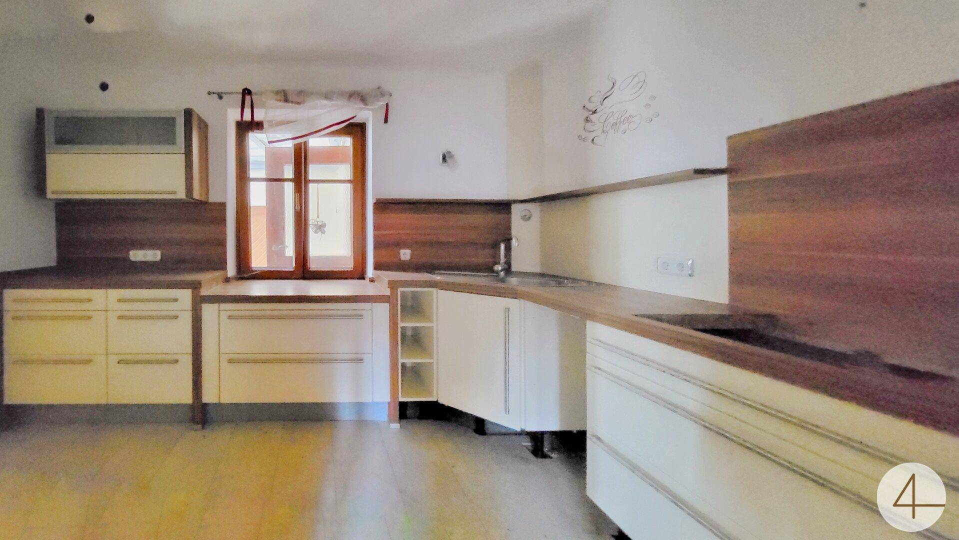 Einbauküche mit hellen Fronten, Holzdetails und Fenster über der Spüle.