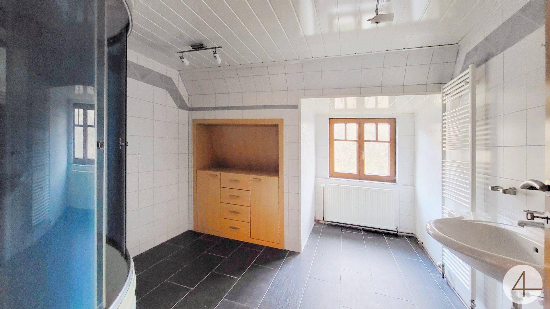 Badezimmer mit Duschkabine, Waschbecken und Fenster, gefliest in Weiß und Dunkelgrau.