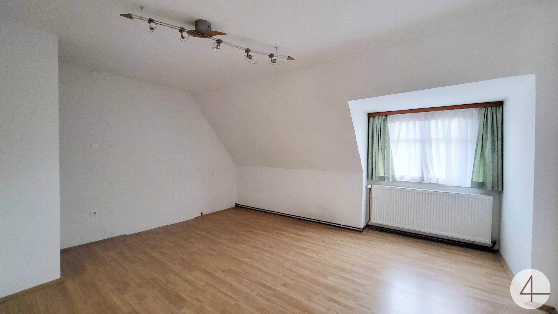 Schlafzimmer im Dachgeschoss mit Holzboden, schräger Decke und Fenster mit Heizkörper.