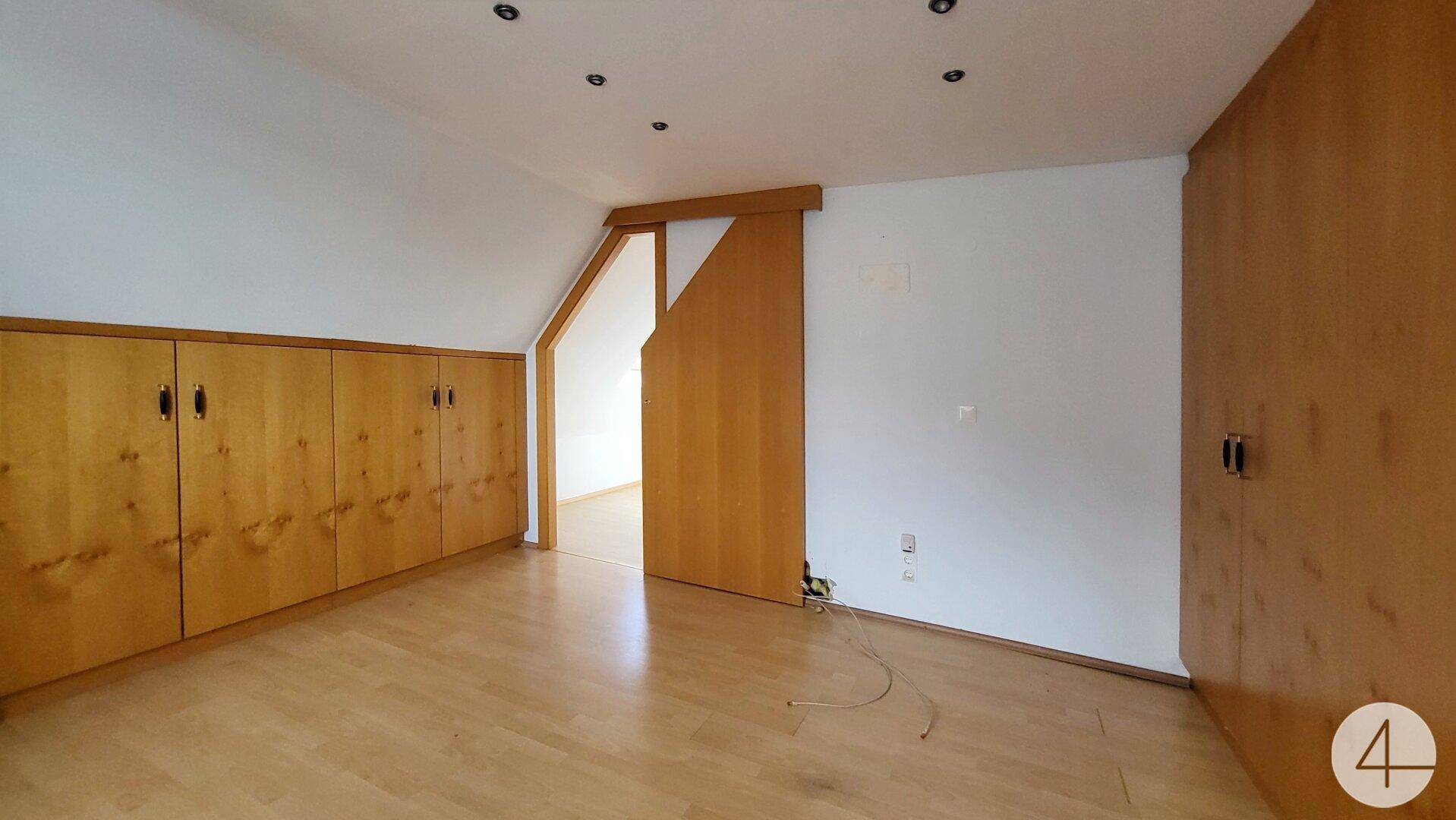 Dachgeschoss-Schlafzimmer mit Einbauschränken aus Holz und Zugang zu einem weiteren Raum.