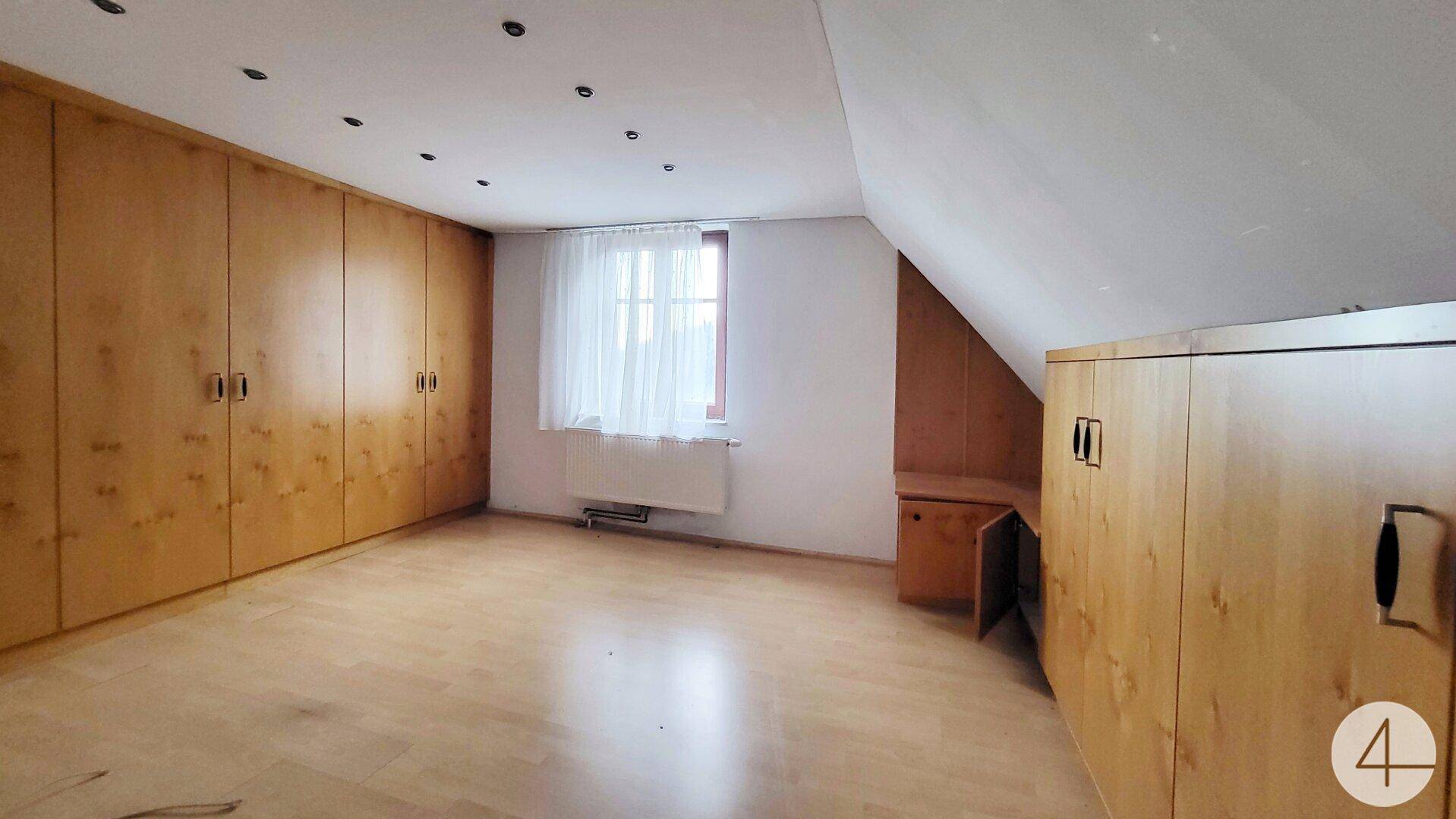 Helles Schlafzimmer im Dachgeschoss mit Einbauschränken und Fenster.