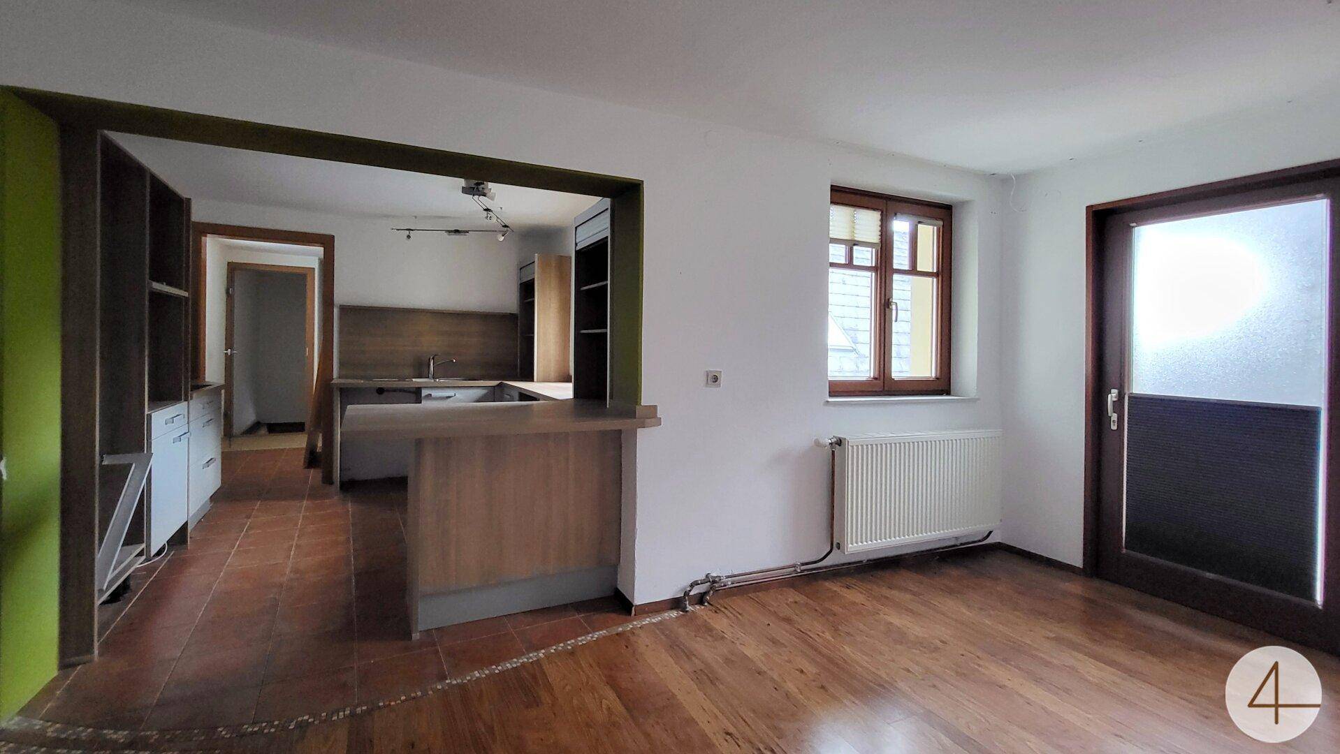 Wohnbereich mit Holzboden, Bartheke und Blick in die angrenzende Küche.