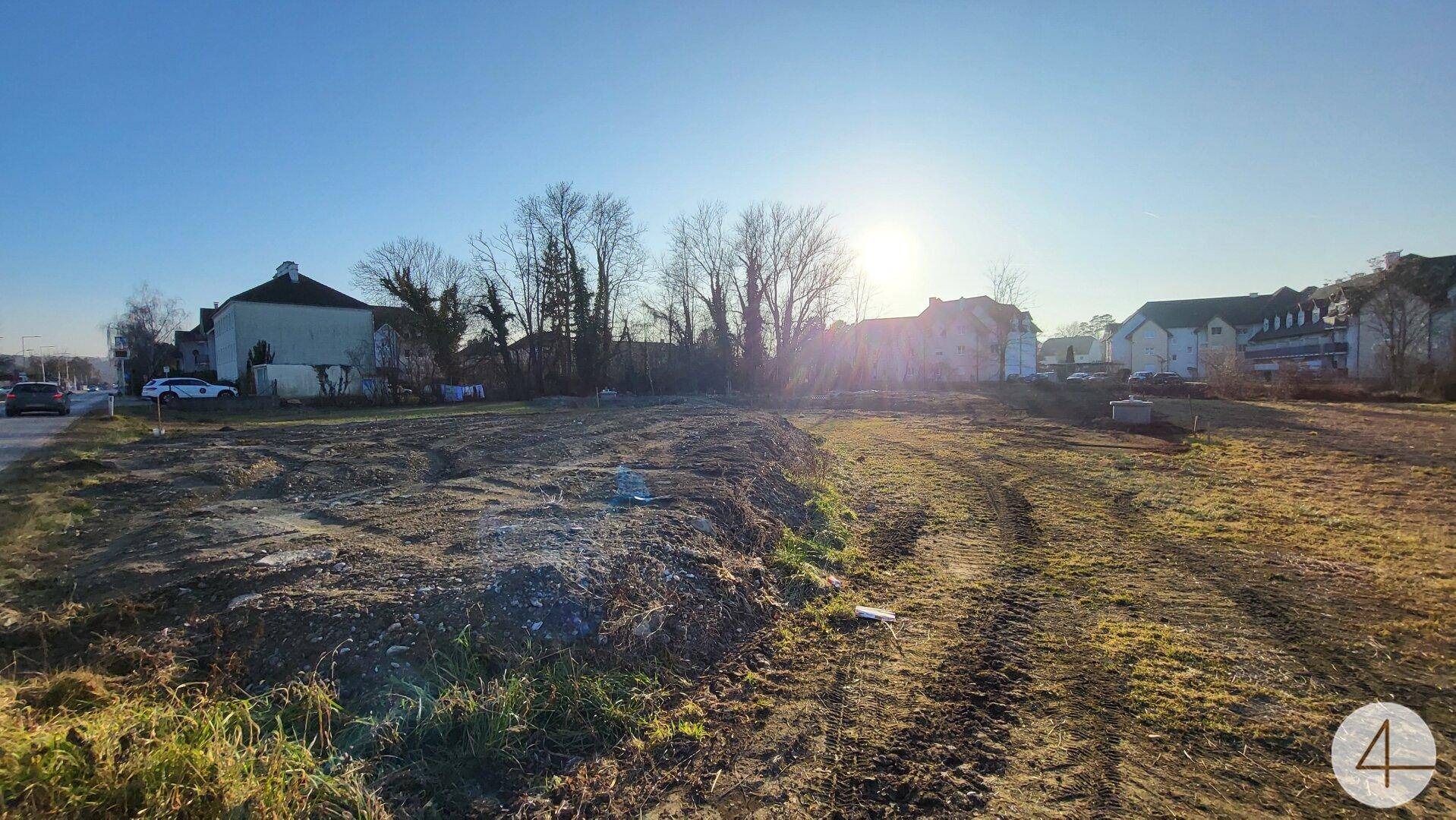 Sonniges Baugrundstück mit weitem Blick und angrenzender Straße unter klarem Himmel.
