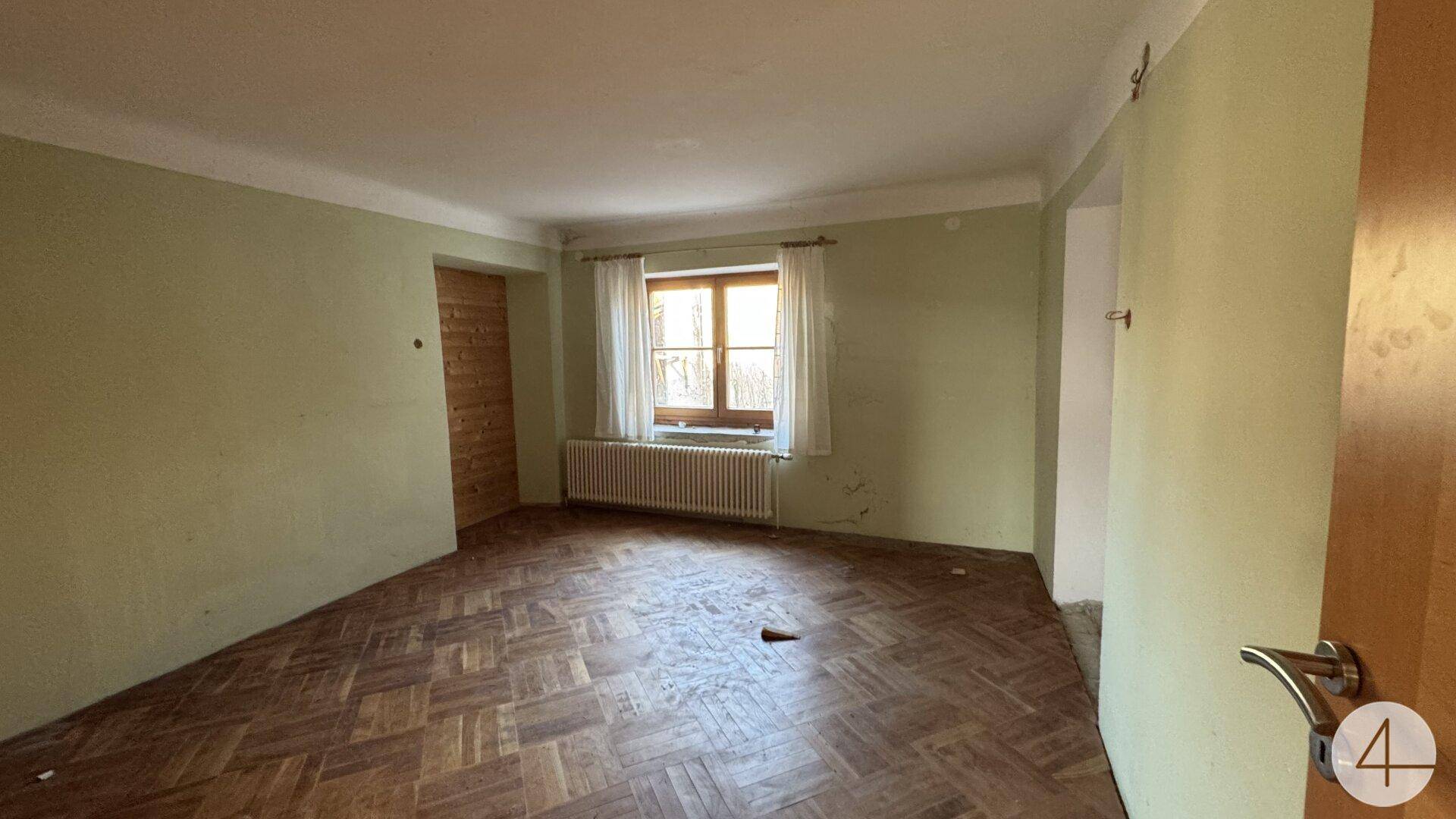 Wohnraum mit grün gestrichenen Wänden, Parkettboden und einem Fenster mit Heizkörper.