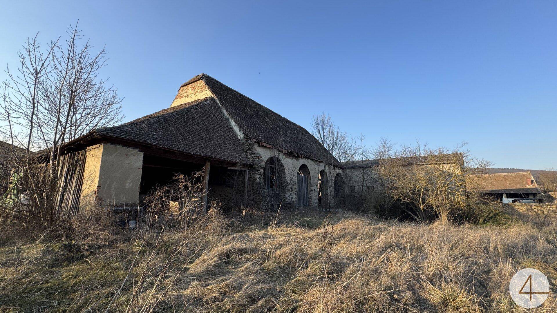 Altes Scheunengebäude mit charakteristischem Dach und verwitterter Fassade, umgeben von trockenem Gras.