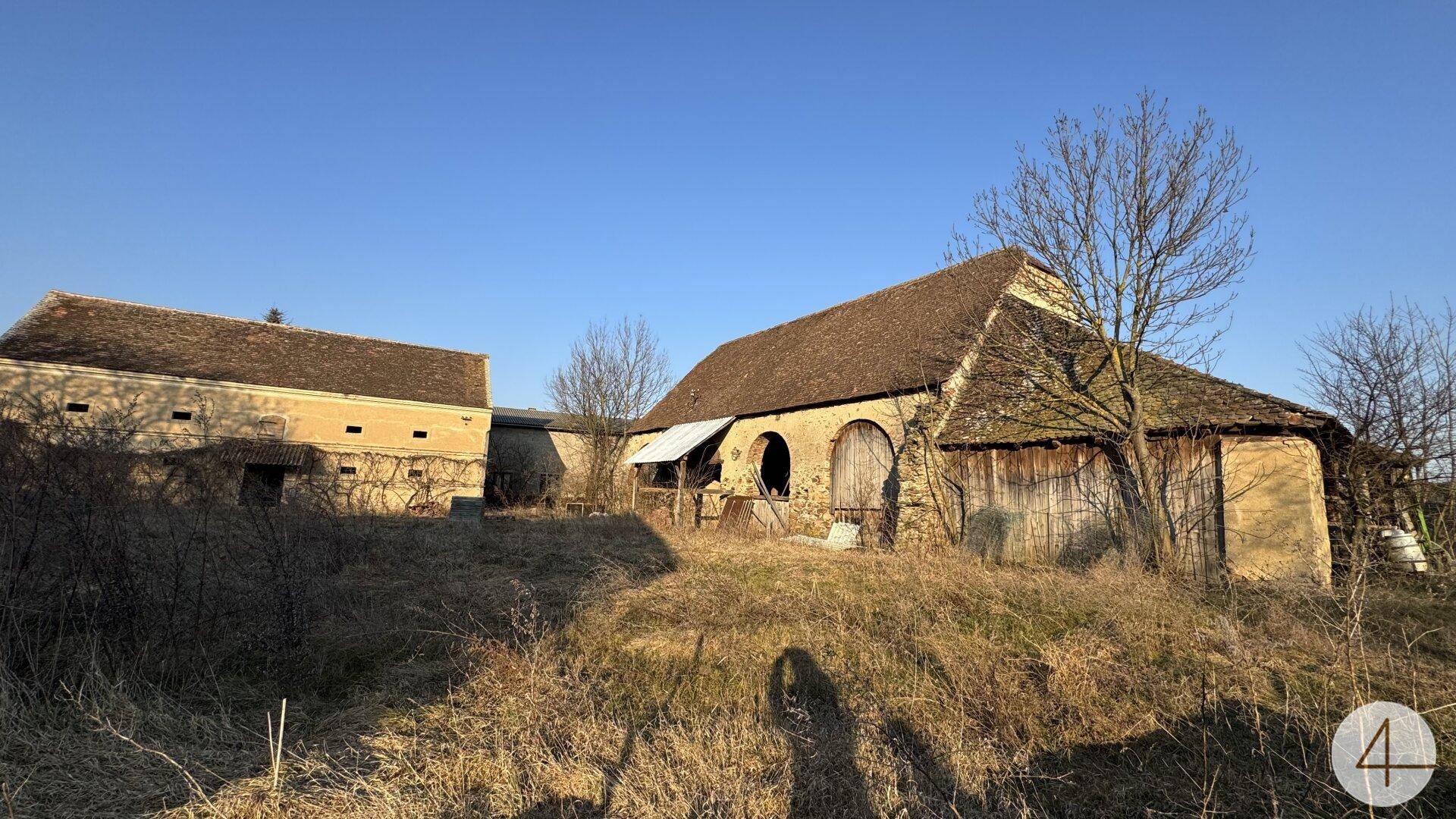 Ländliches Anwesen mit zwei historischen Gebäuden und weitläufigem, ungenutztem Grundstück bei Sonnenlicht.