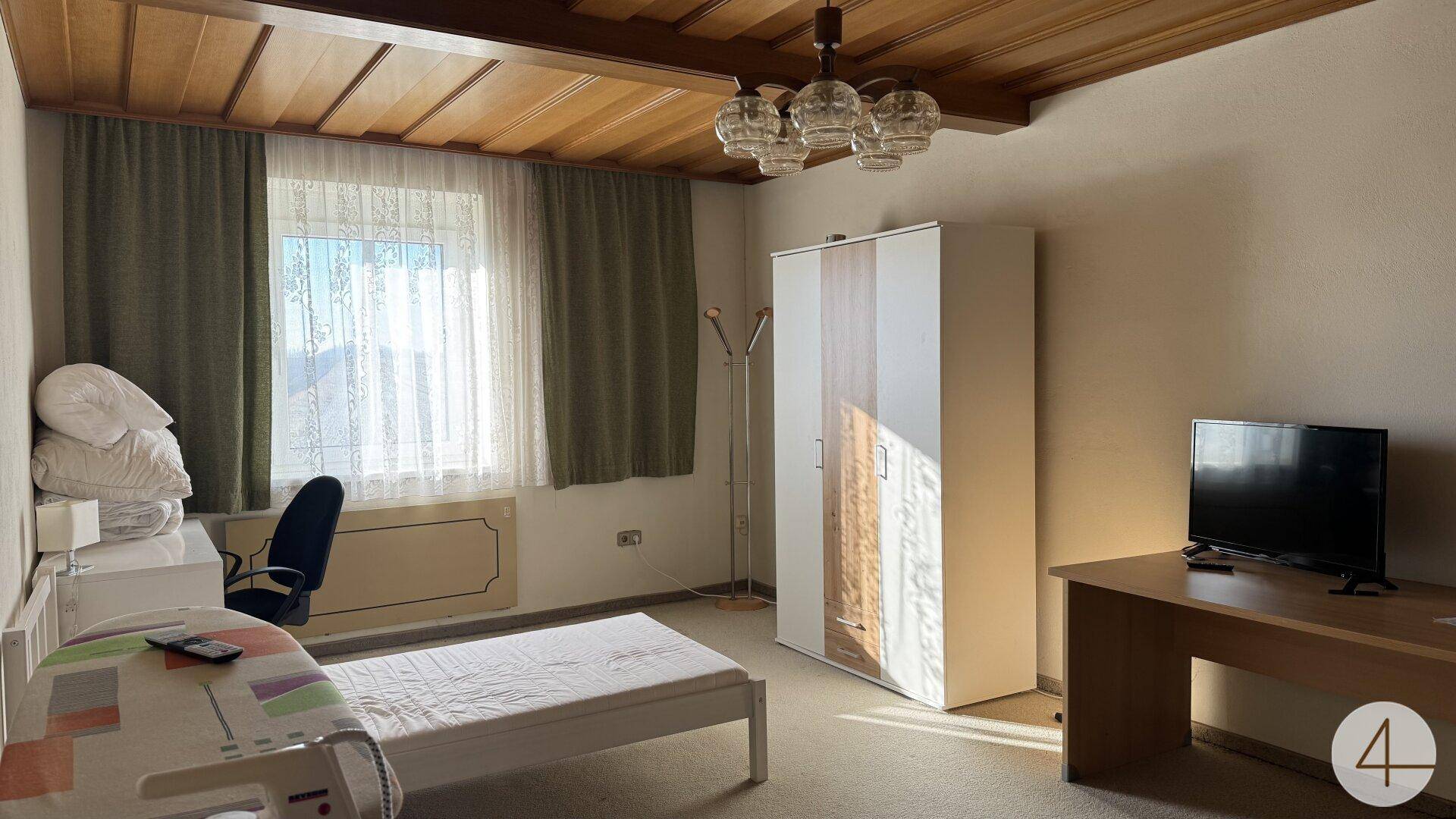 Schlafzimmer mit Einzelbett, Kleiderschrank, Schreibtisch und Holzdeckenverkleidung.